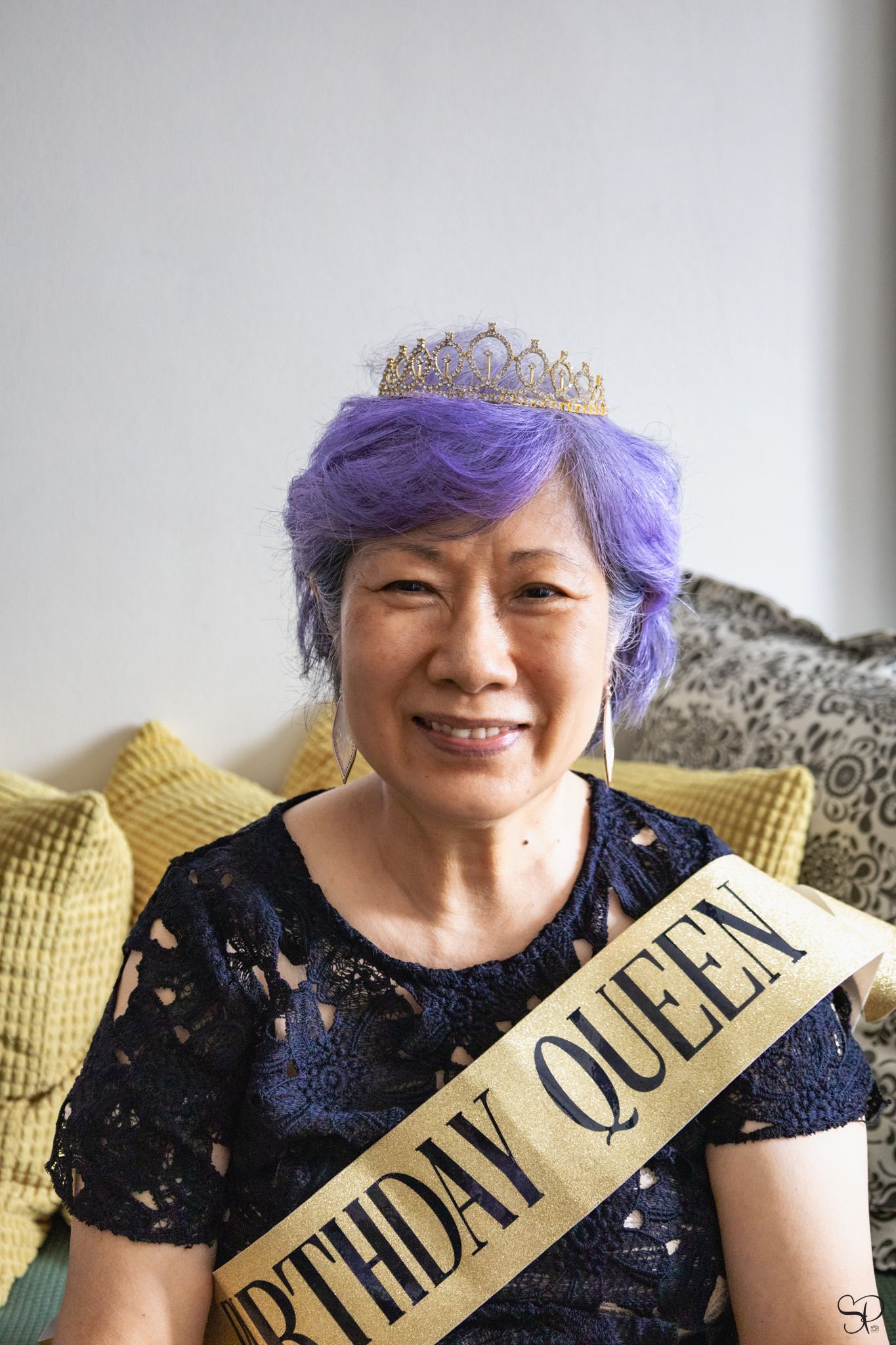 A picture by Sara Pang (MSK Productions) of an elderly woman with purple hair wearing a golden crown and a golden birthday queen sash.