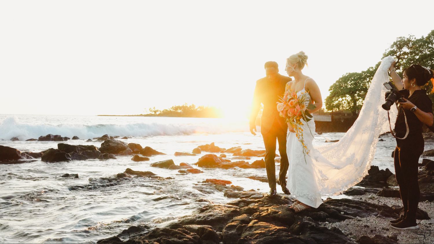 A photo of videographer Sara Pang (MSK Productions) as she holds up a bride's gown on the beach of Papa Kona's in Kona, Hawai'i.