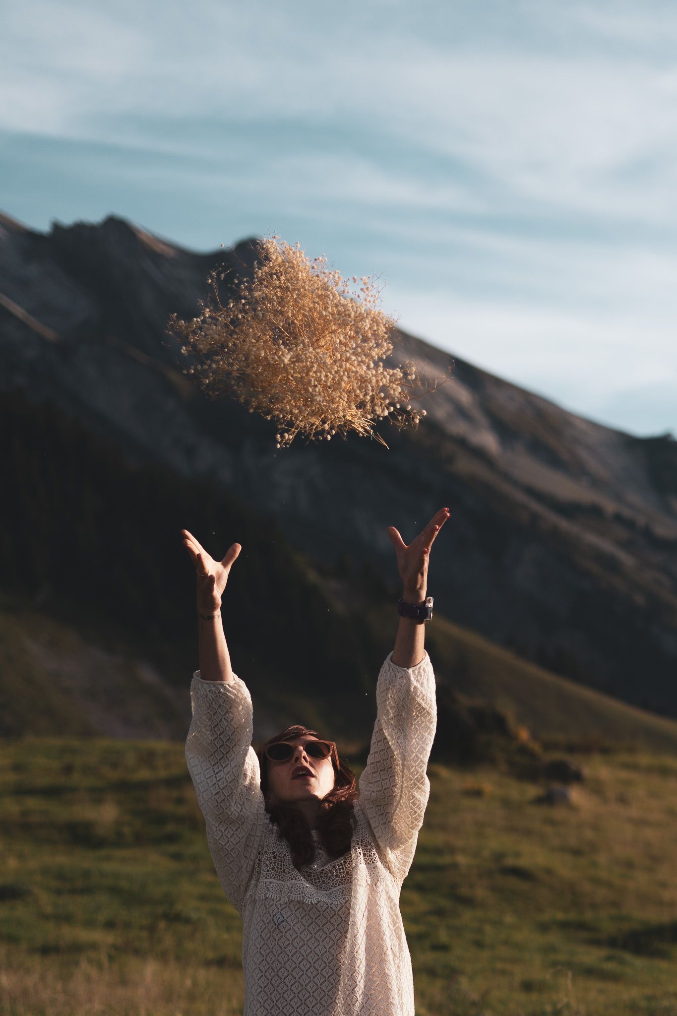 Femme qui jète un bouquet de fleurs séchées en montagne avec la lumière dorée du soleil couchant, proche d'Annecy.