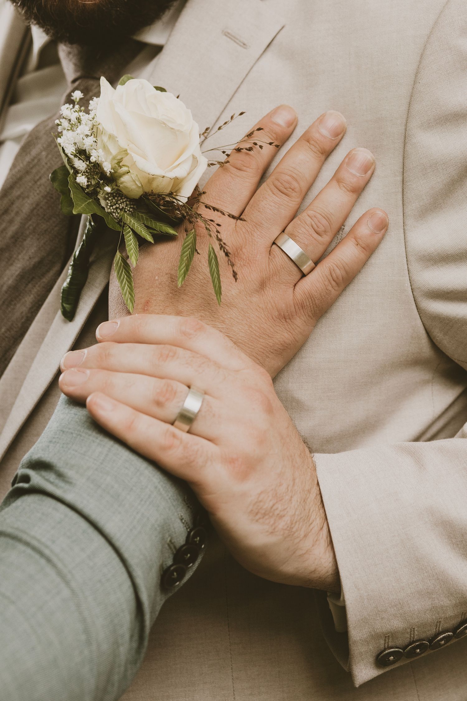 Close-up of wedding rings and a white rose boutonniere against a light colored suit.