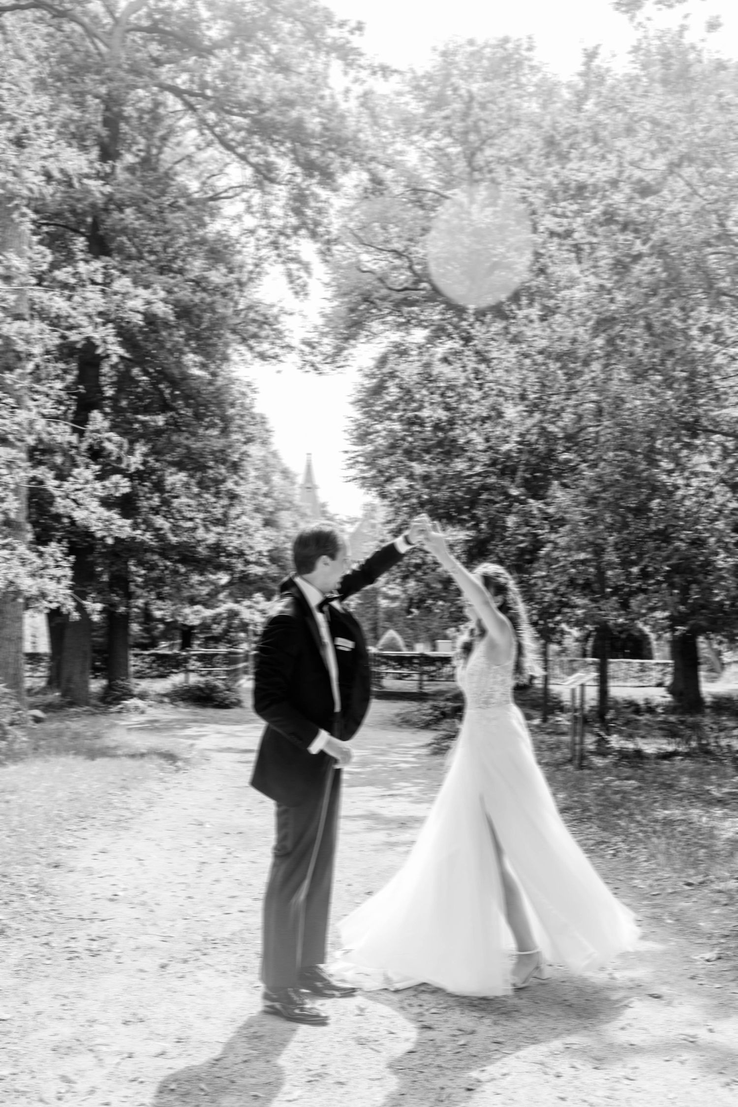 Black and white photo of bride and groom releasing a heart balloon outdoors among trees on their wedding day.