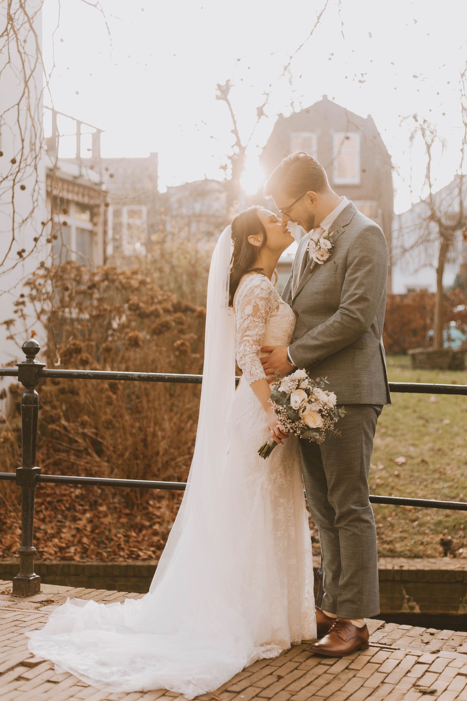 A romantic wedding couple embraces on a wooden deck during sunset with autumn foliage in the background.