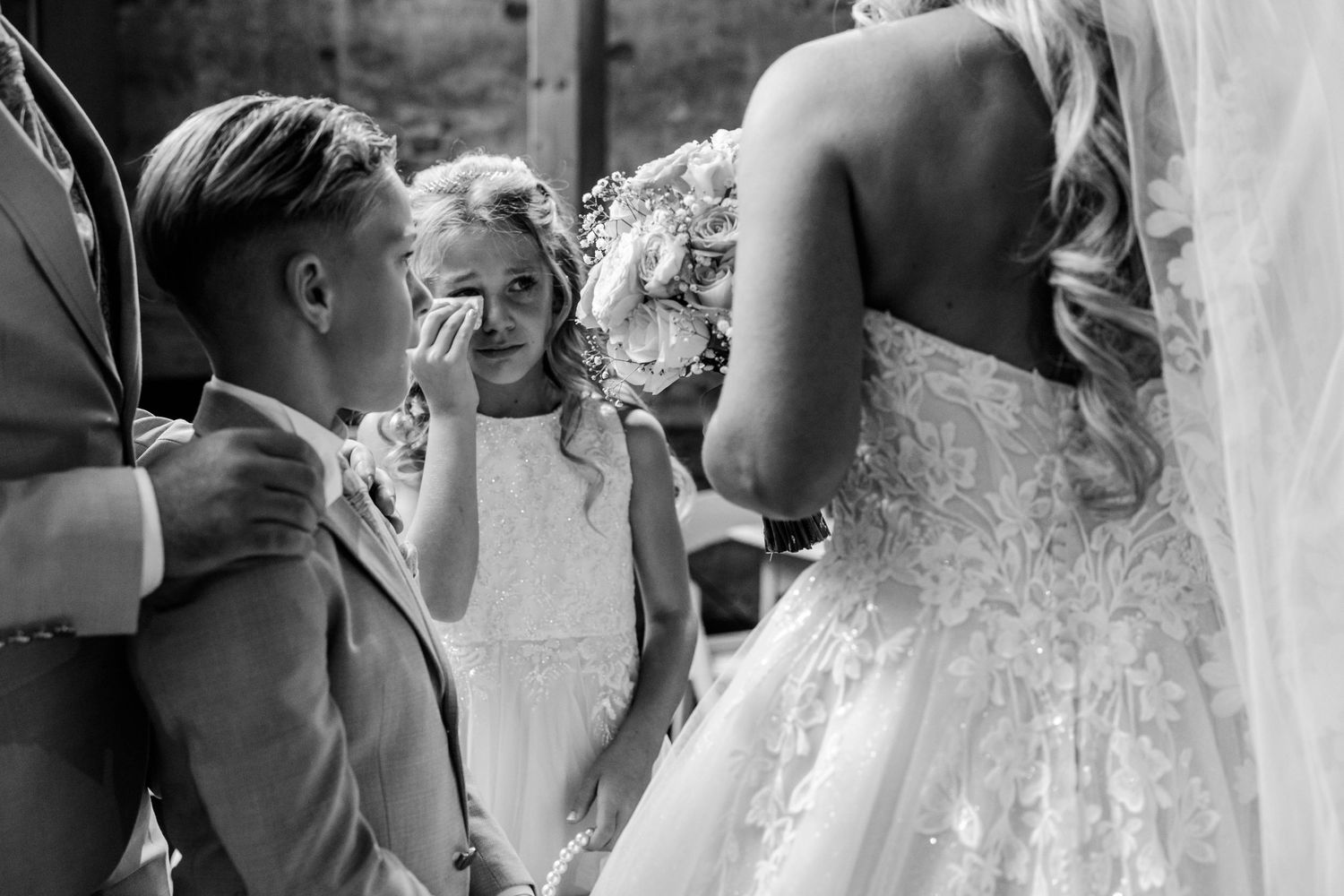 Black and white photo of children crying at a wedding, with a flower girl wiping tears beside the lace-gowned bride.