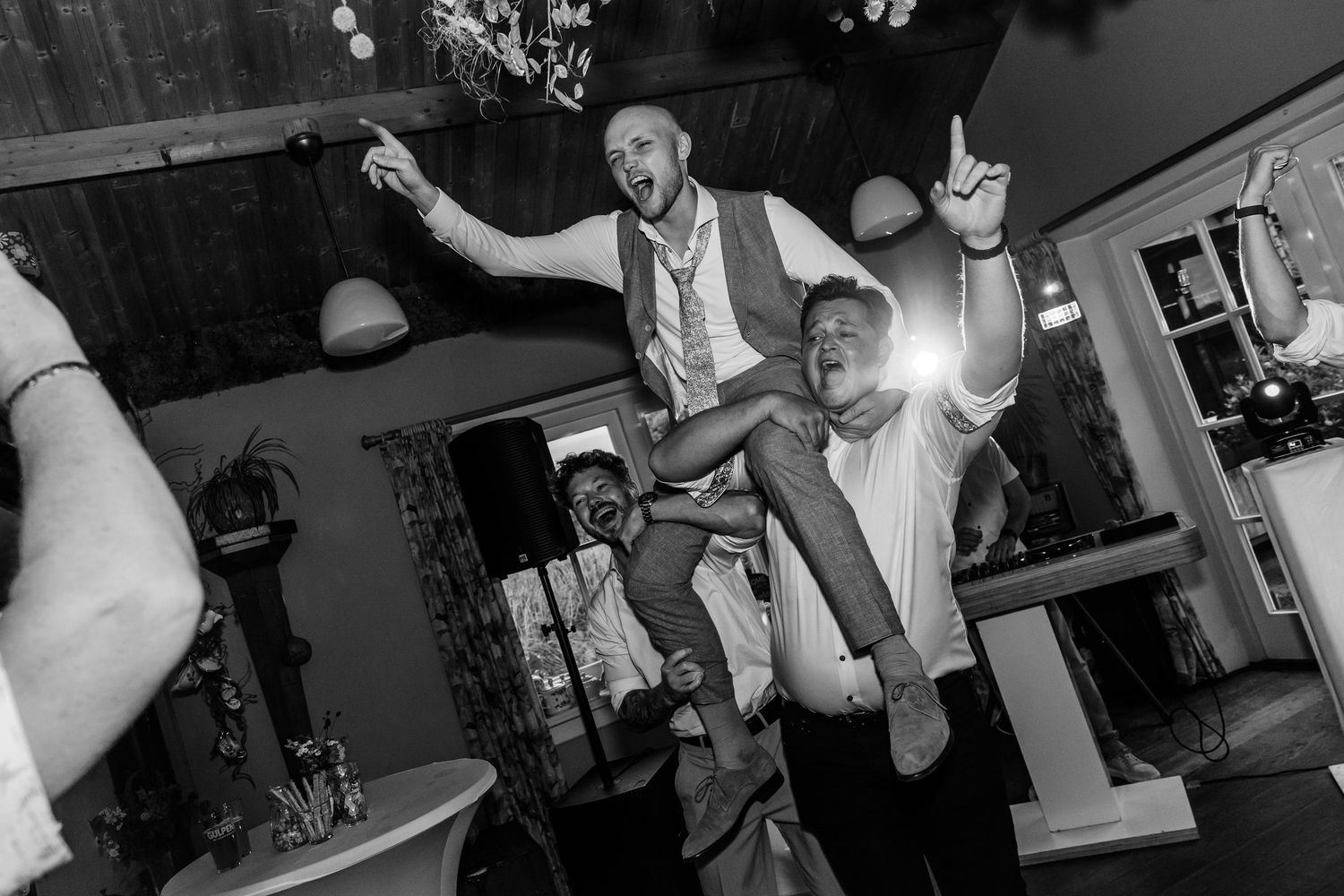Groom lifted by guest during lively wedding reception dance party in black and white photo.