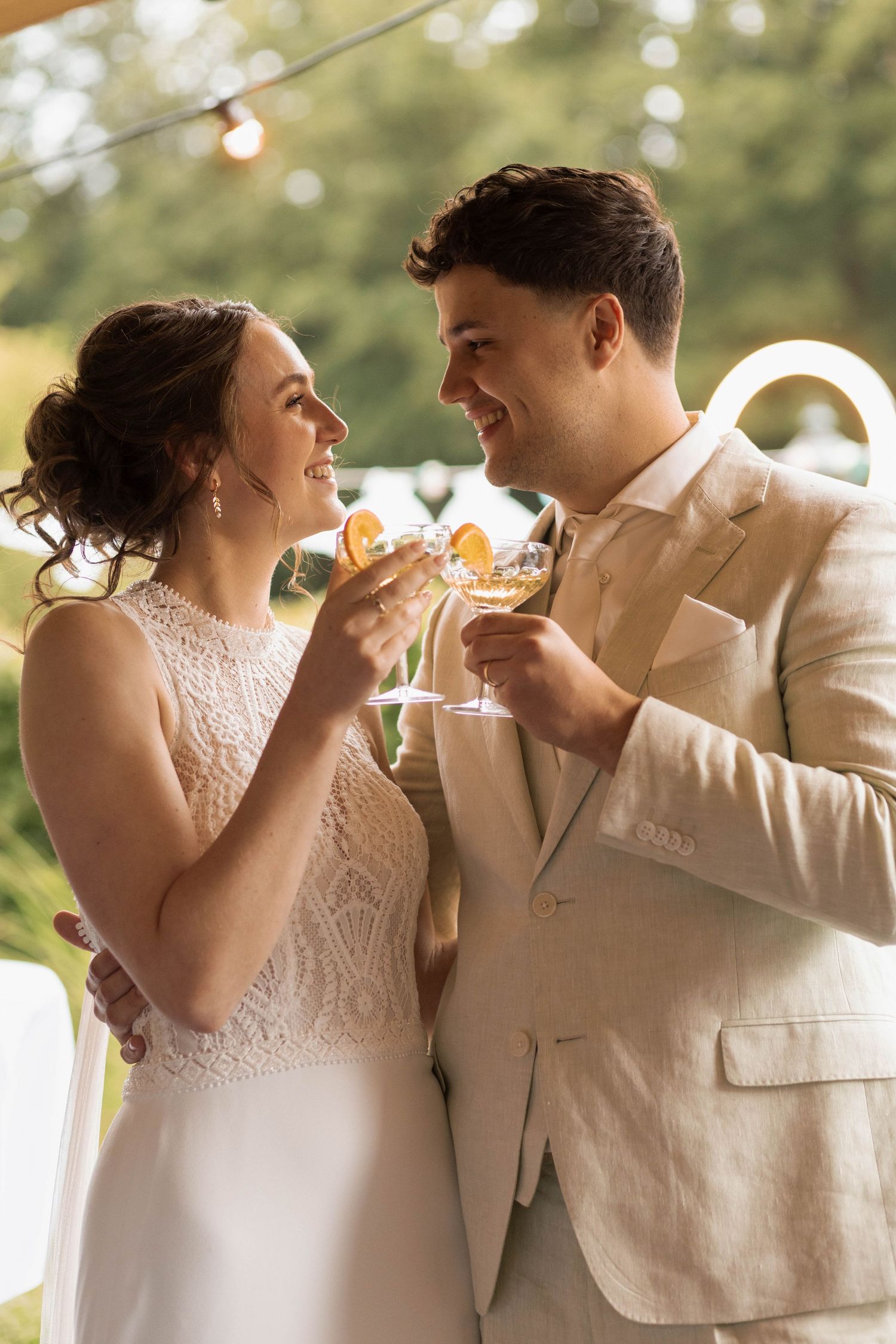 Smiling bride and groom toasting with champagne glasses at outdoor wedding reception.