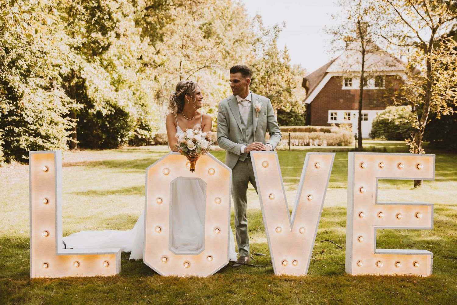 Outdoor wedding photo shoot in a garden setting with blush pink letter signs spelling out LOVE in golden sunlight.