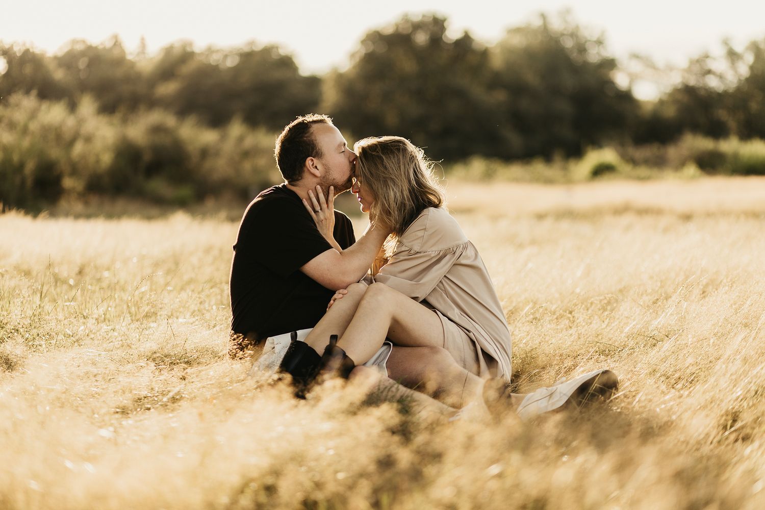 A couple shares an intimate moment while sitting together in a golden wheat field at sunset.