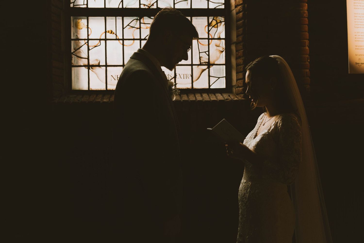 A silhouetted couple stands in a dark room with light streaming through a window creating a moody atmosphere.