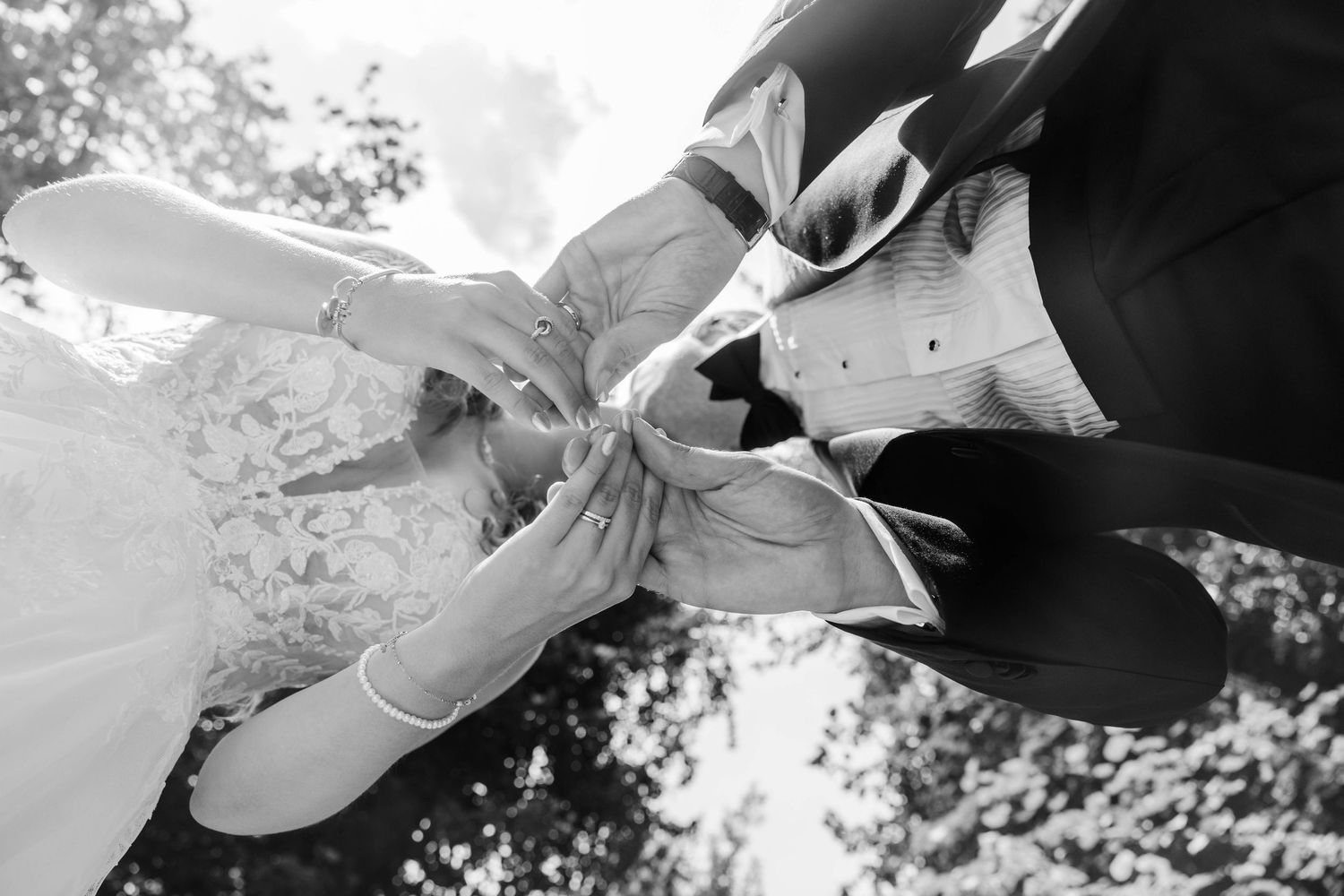 Black and white photo of bride and groom exchanging wedding rings during outdoor ceremony.