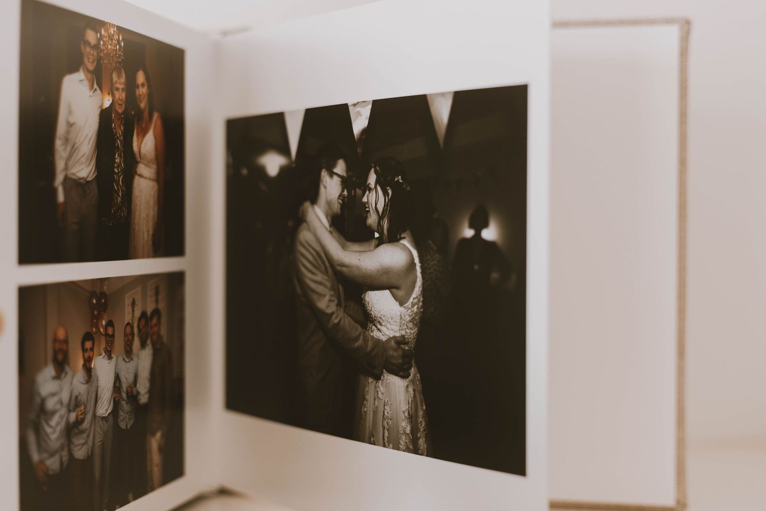 Wedding photo album open displaying black and white couple embracing and color group photos on white pages.