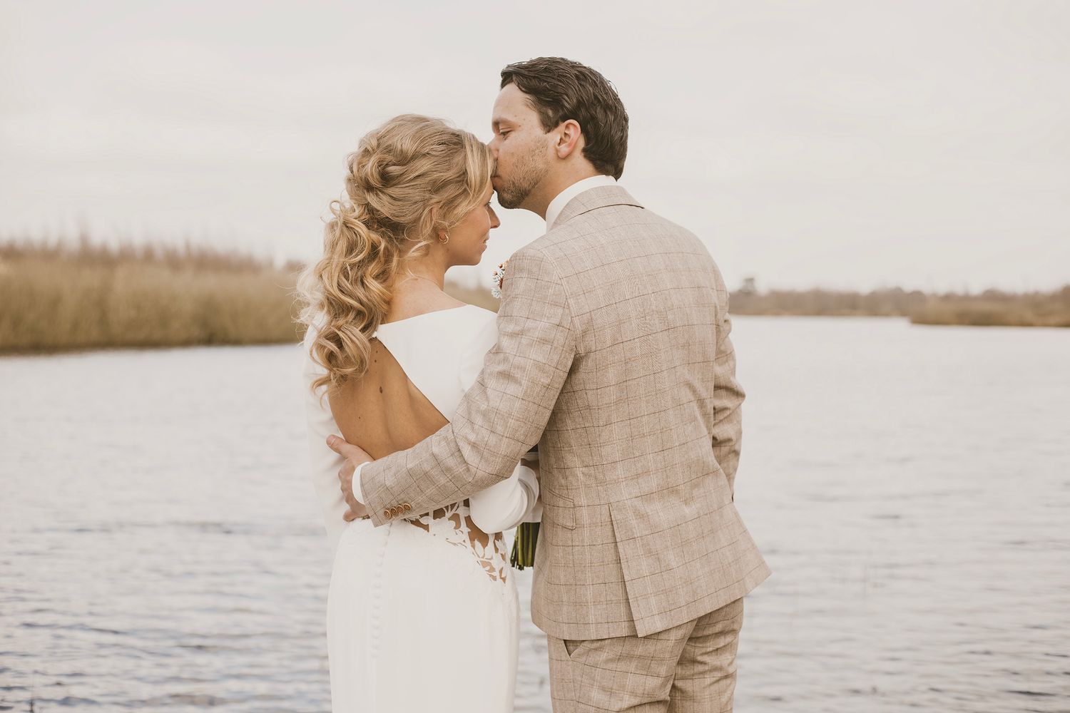 Romantic couple embraces on a dock overlooking a serene lake during sunset in autumn.