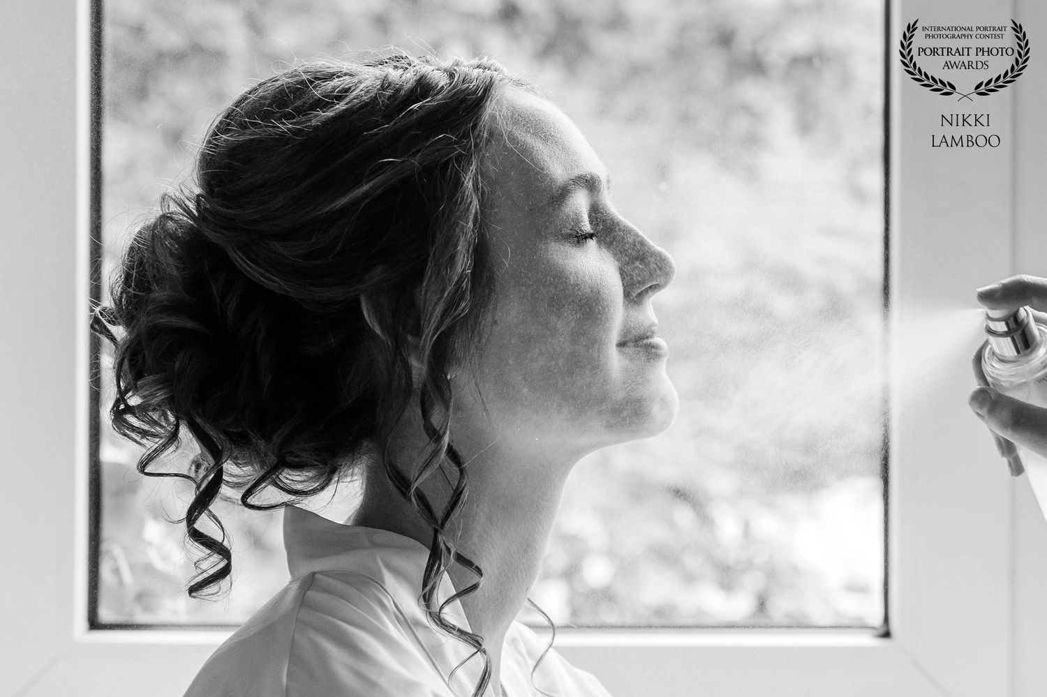 Black and white bridal portrait of elegant woman with updo hairstyle gazing out window in soft natural light.