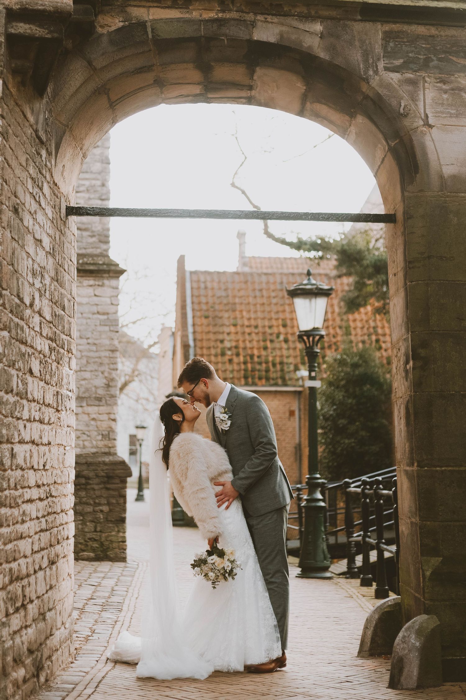A romantic wedding couple shares intimate moments under stone archways in an elegant outdoor setting.