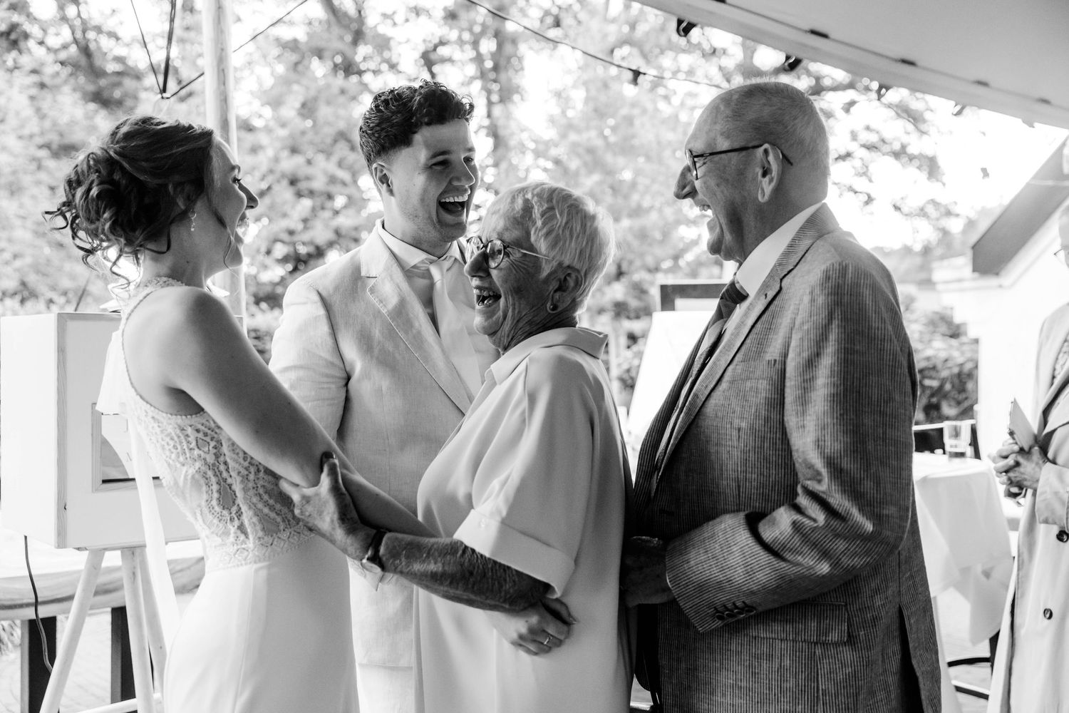 Black and white photo of a bride and groom laughing with elderly guests at an outdoor wedding reception.