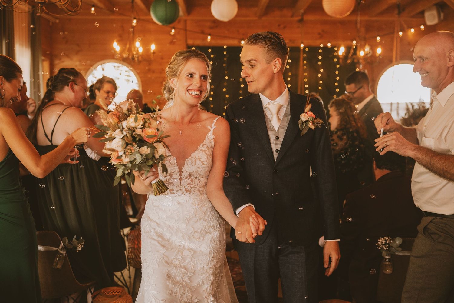 Wedding party celebrates on a dimly lit dance floor decorated with string lights and balloons during reception.