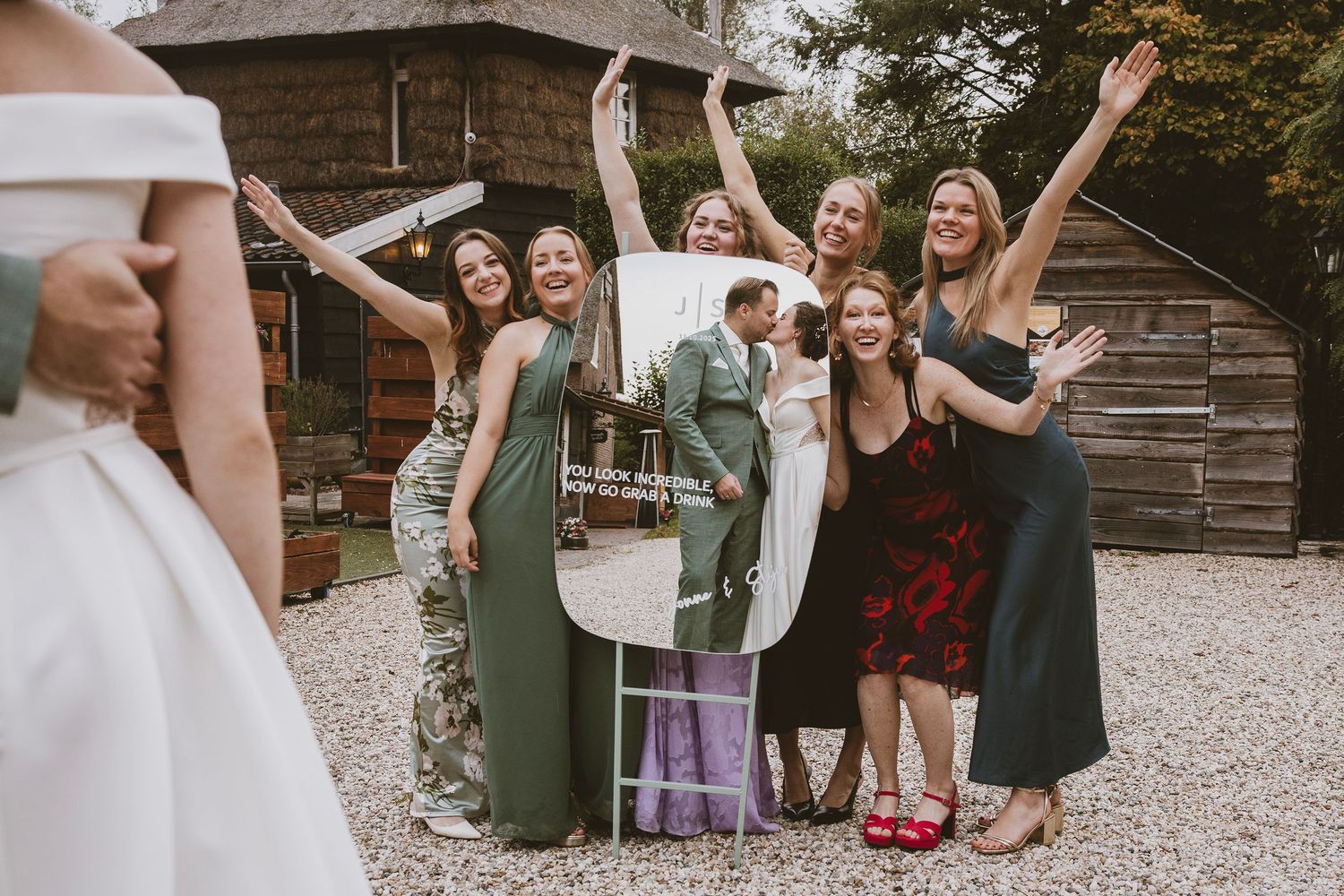 Bridesmaids in colorful dresses cheering and posing with a bride outside a rustic barn venue at a wedding celebration.