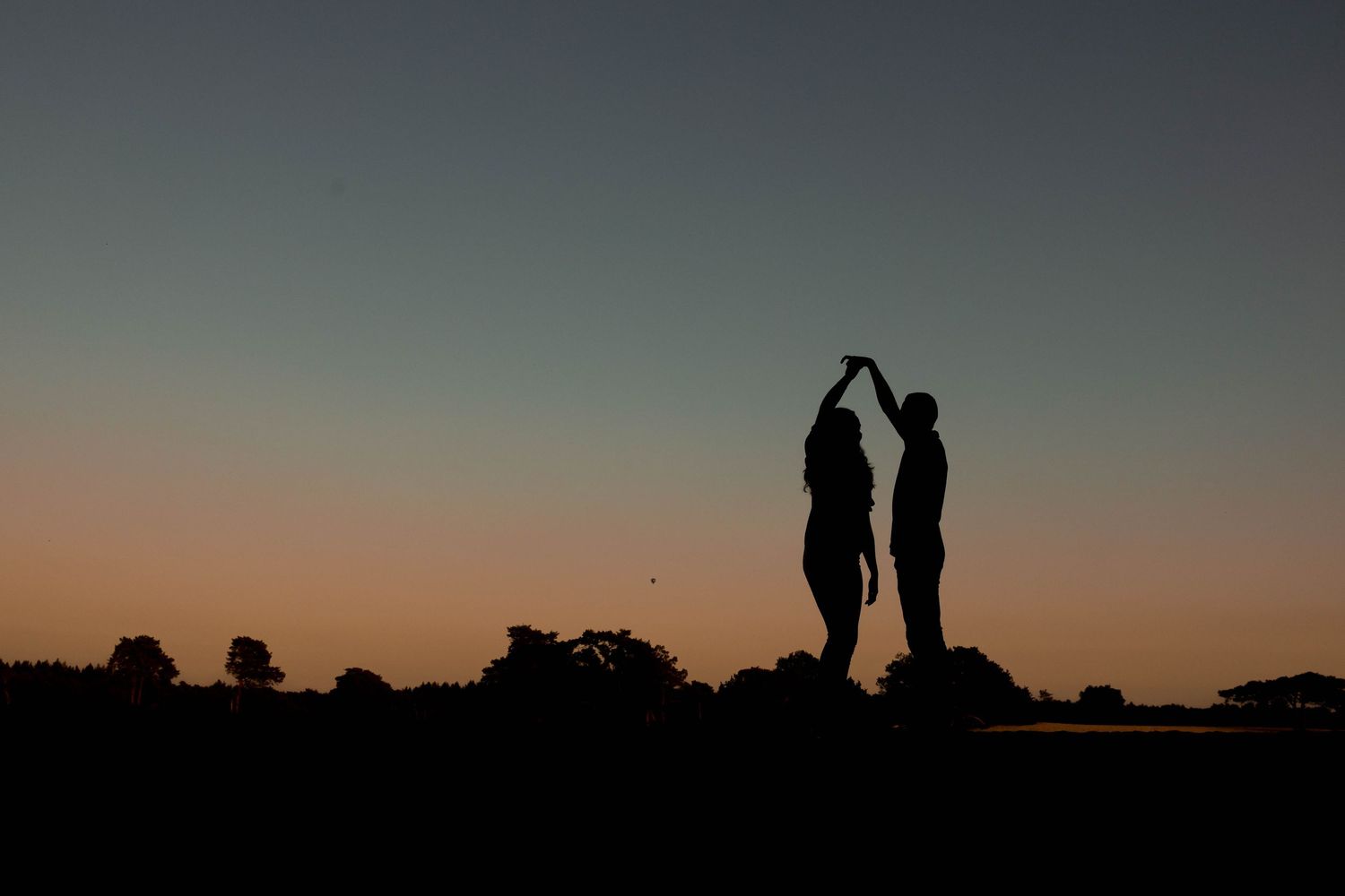 Silhouette of a couple dancing at sunset with a colorful sky and tree line in the background.