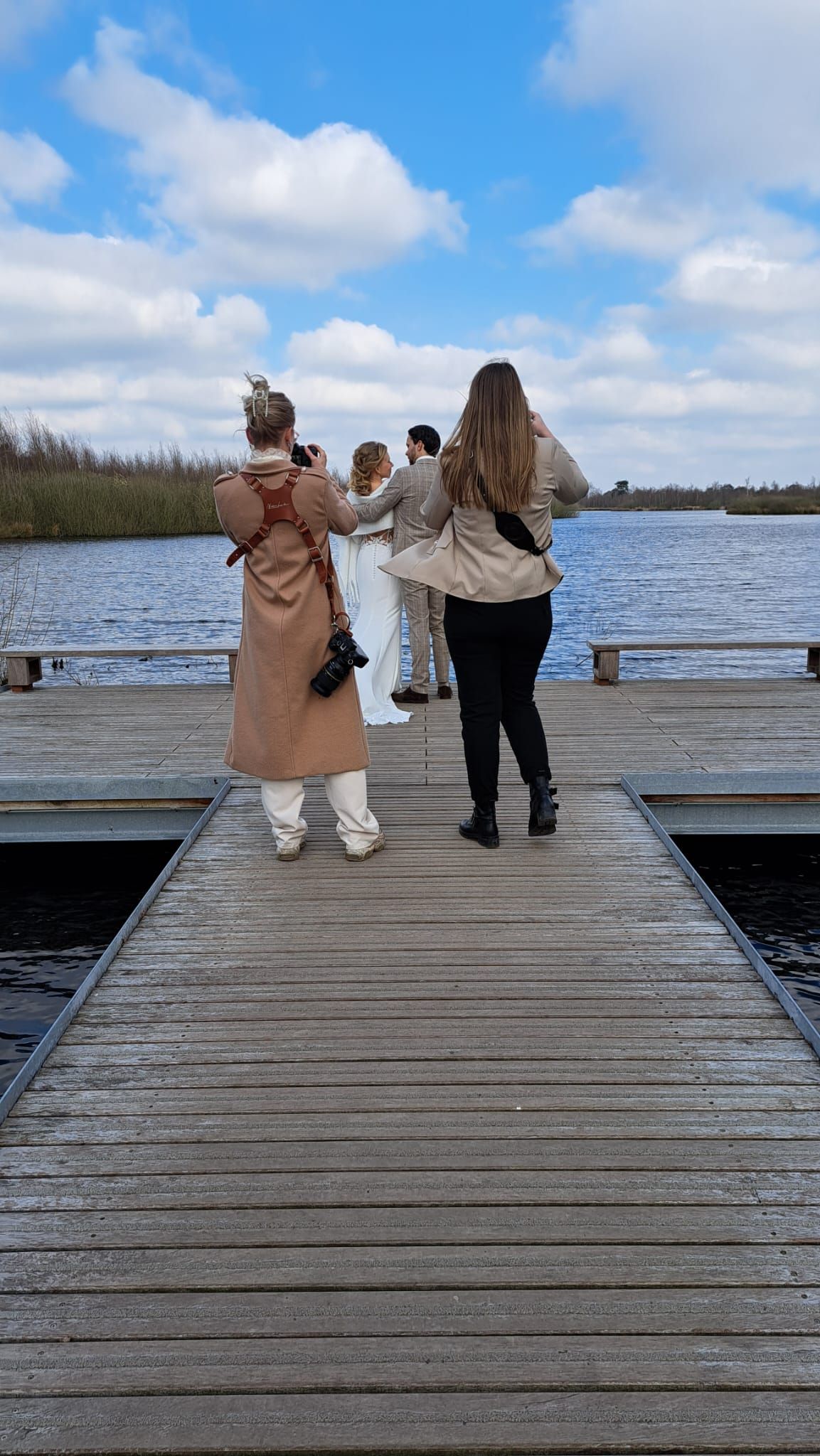 Group of people standing on a wooden dock overlooking a calm lake under a partly cloudy sky.