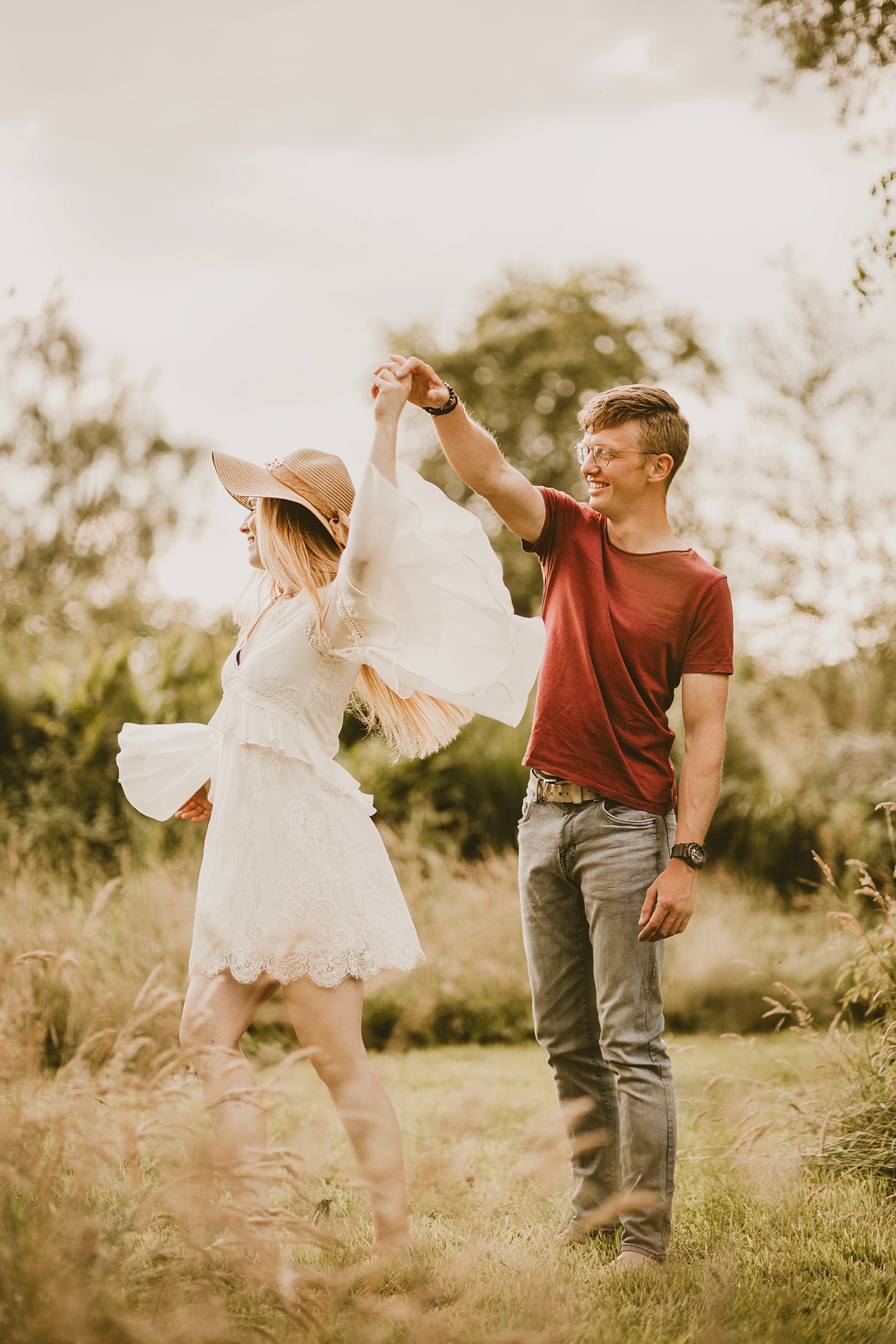 A couple dances playfully in a sunlit meadow wearing casual clothing and creating joyful movements together.
