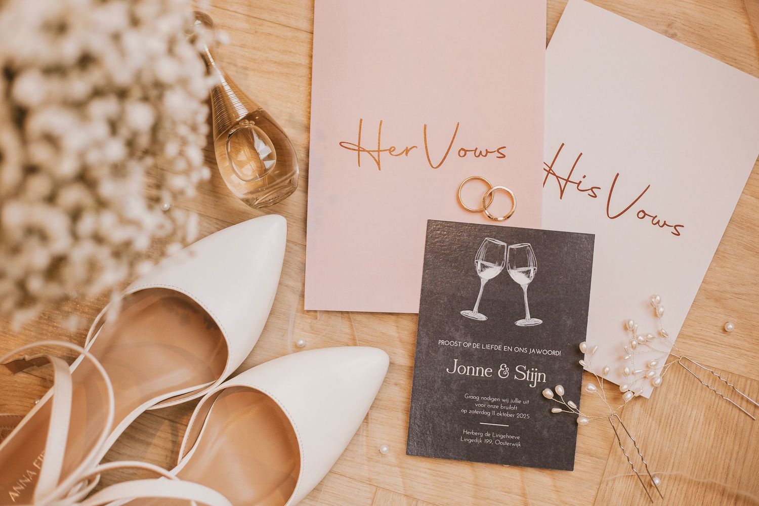Wedding stationery and place cards arranged on a pink surface with champagne glasses.