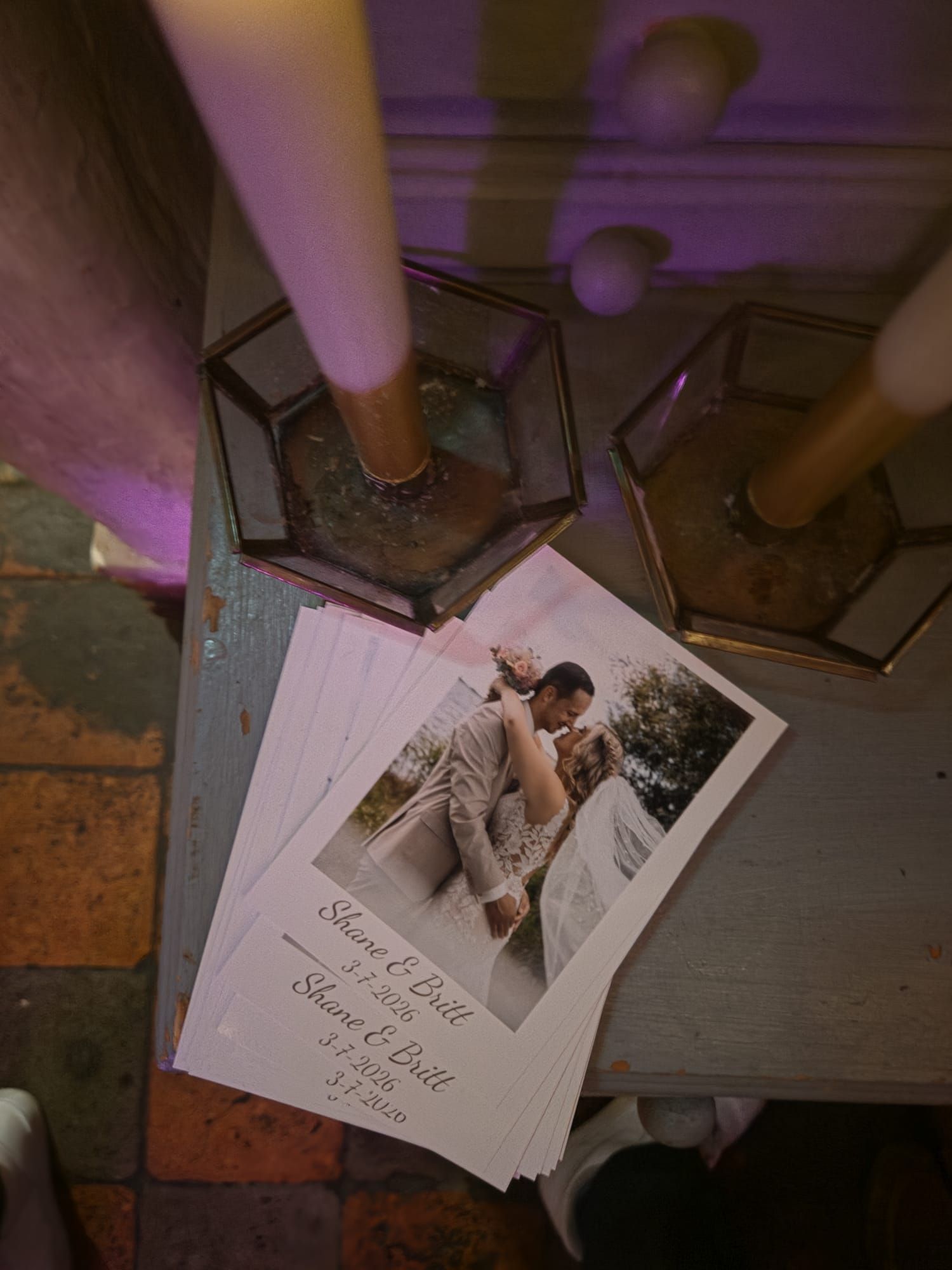 Wedding photo cards for Shane and Brill displayed on a wooden table beside geometric candle holders with lit candles.