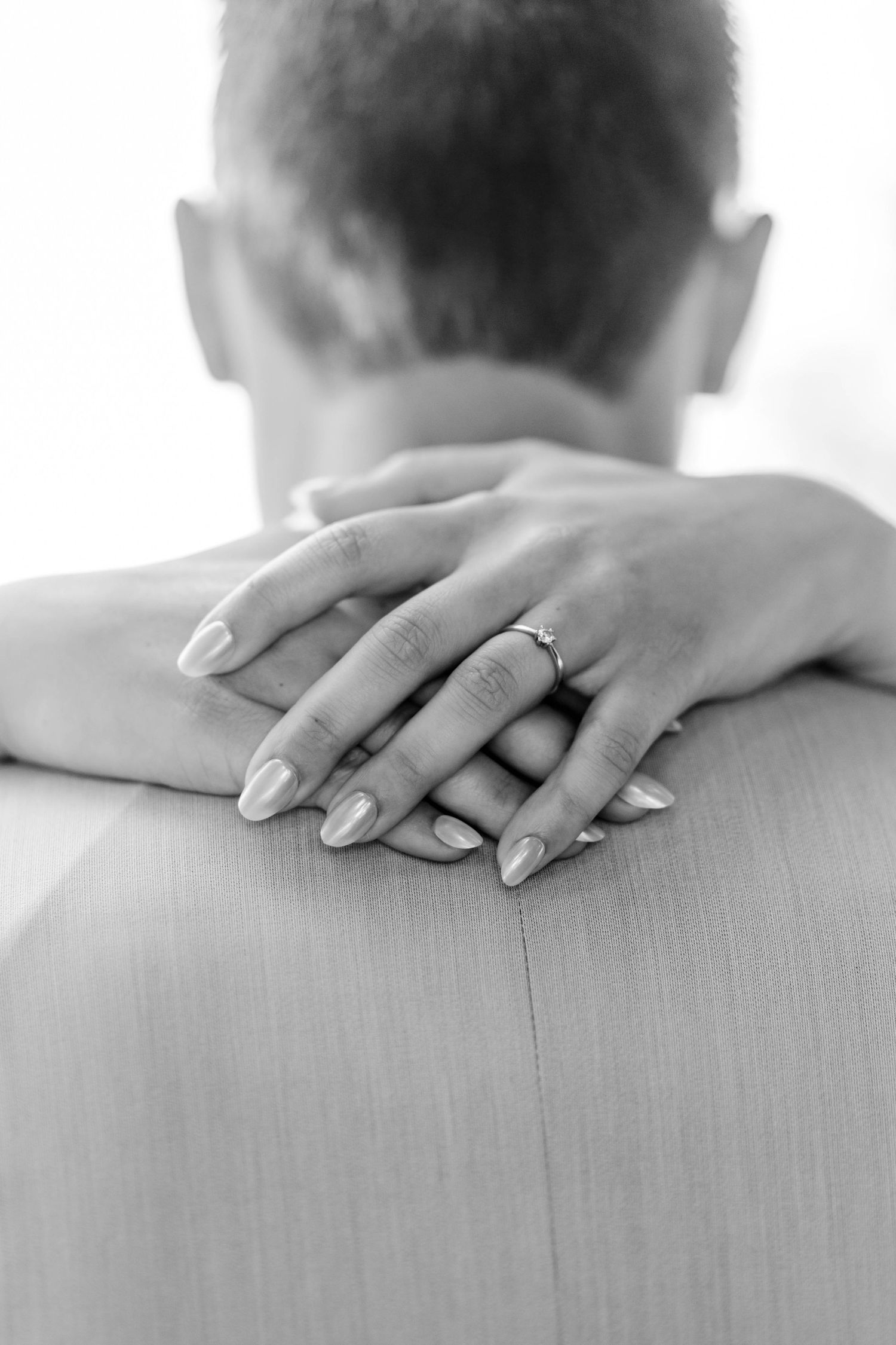 Black and white photo of a bride resting her hands on groom's shoulder, showing wedding ring.