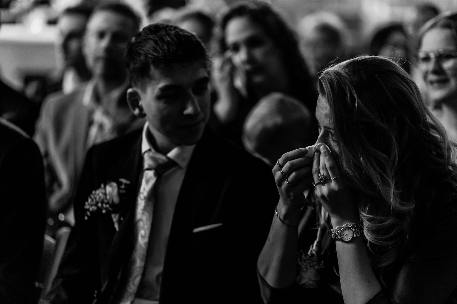 Emotional wedding guest dabbing tears during ceremony in black and white photography.