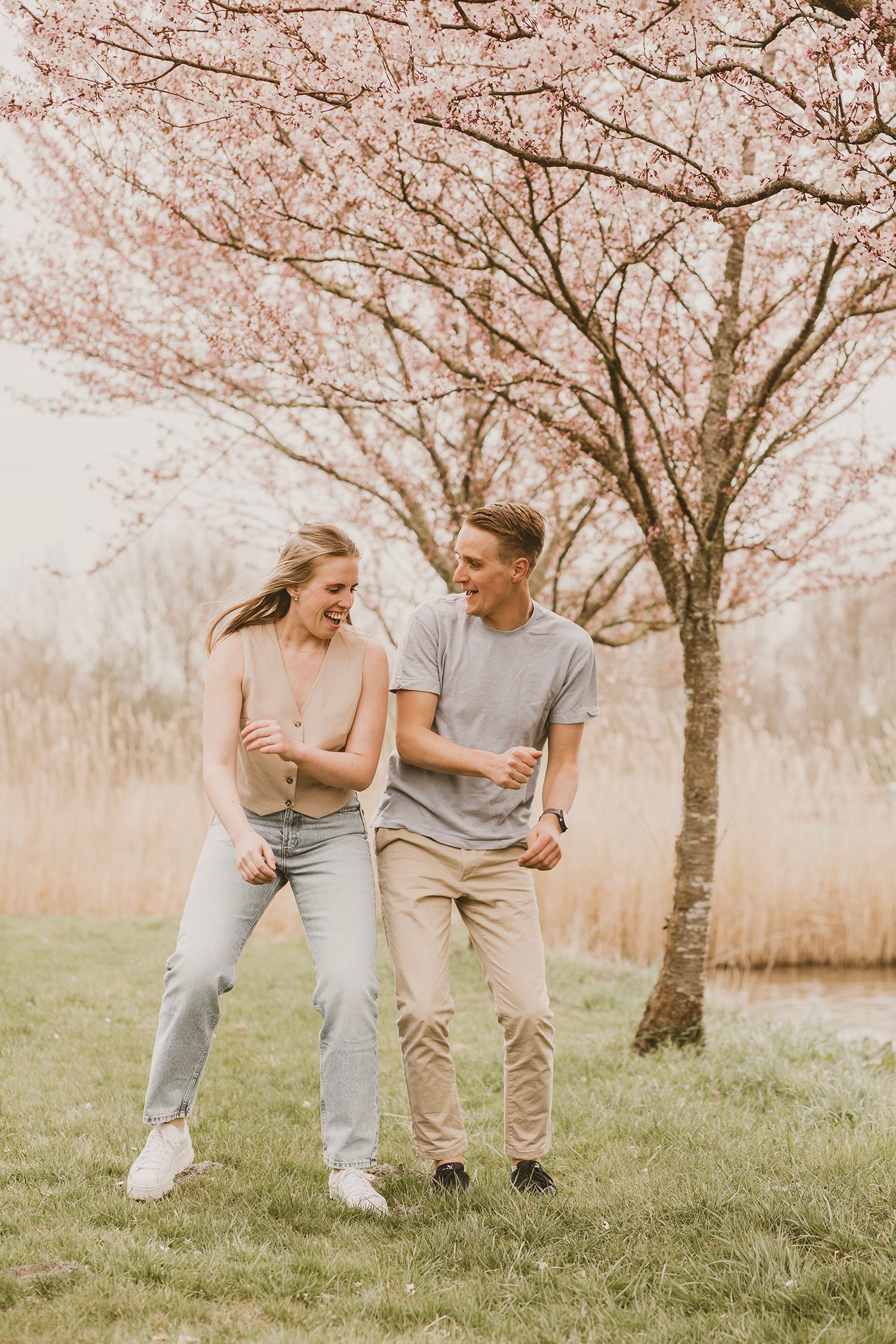 A couple in matching grey outfits share playful moments under blooming cherry blossom trees in a spring meadow.