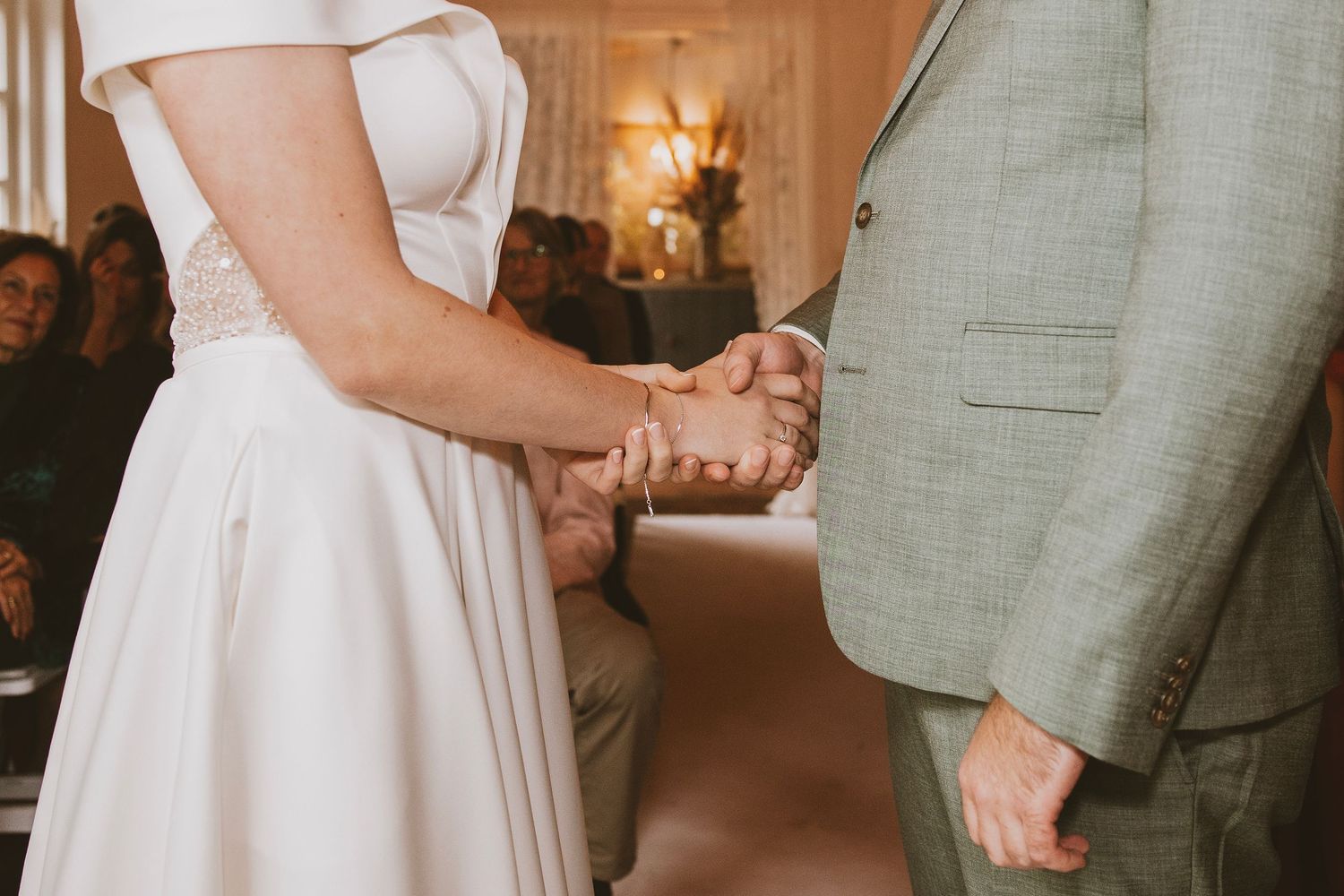 Wedding couple holding hands during reception in sage green and white attire.