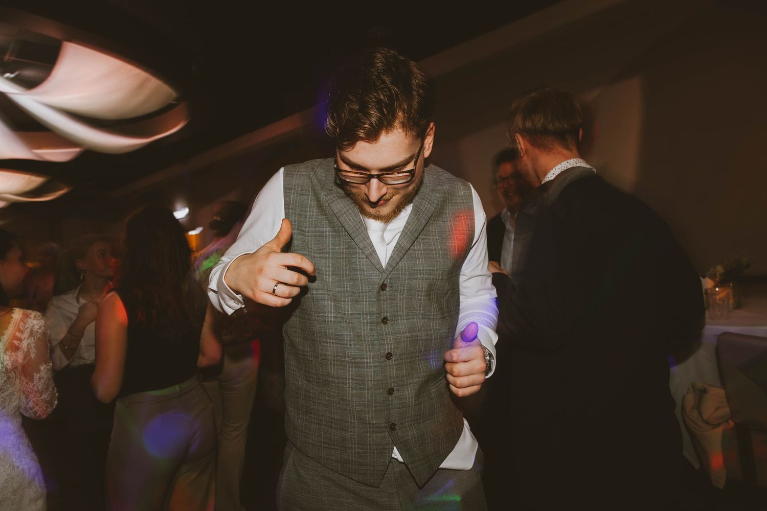 A group of people dancing and celebrating at a lively wedding reception with colorful lighting.