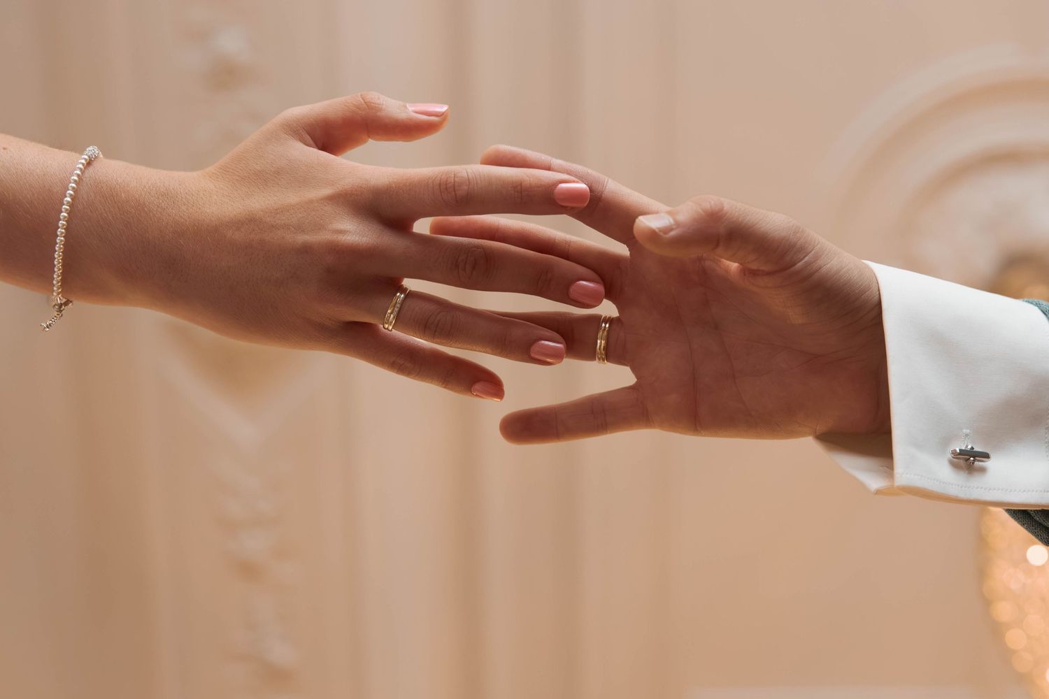 Close-up of two hands touching, woman wearing a diamond engagement ring and bracelet, man in white dress shirt with cufflinks.