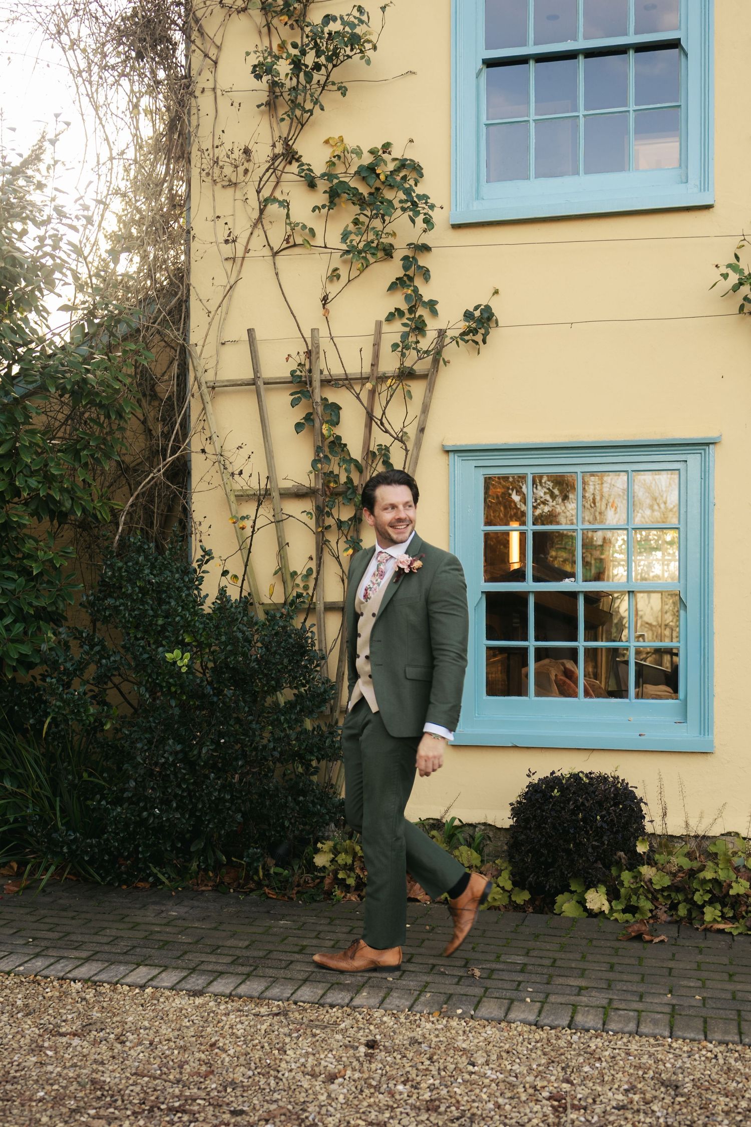 “Groom standing by the blue farmhouse door at South Farm Royston during her wedding day, captured by a UK London wedding photographer.”