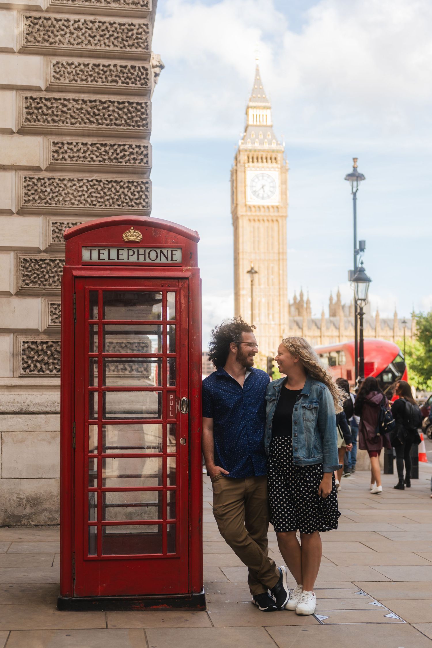 Couple standing beside a red phone booth with Big Ben in the background in Westminster, London captured by UK Photographer @lyfphotos