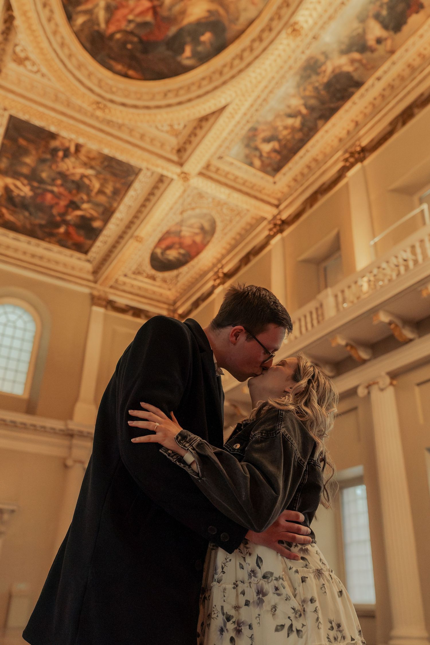 Engaged couple kissing inside Banqueting House London with dramatic ceiling and warm romantic light