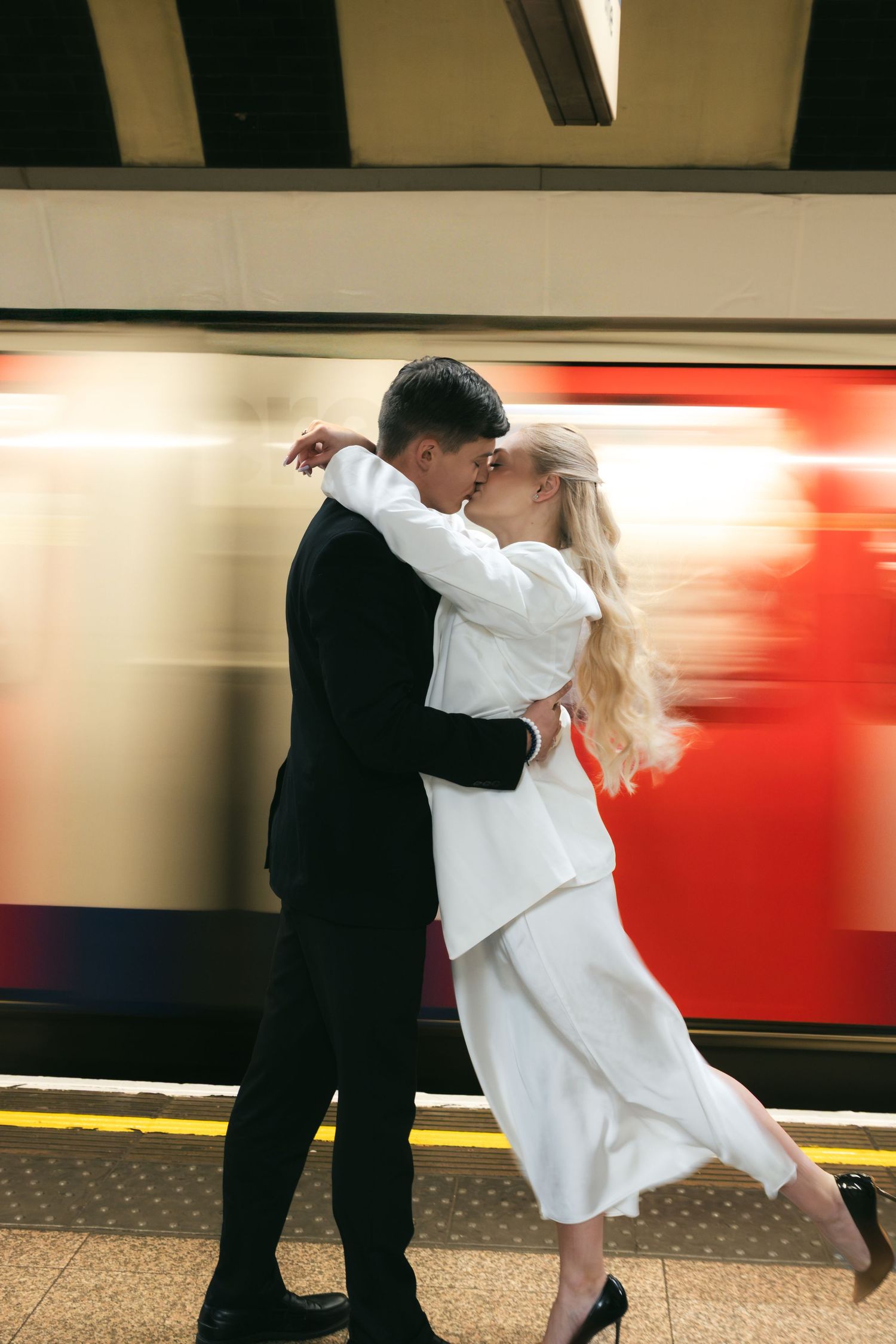 Couple on a London Underground platform with a train passing behind them.