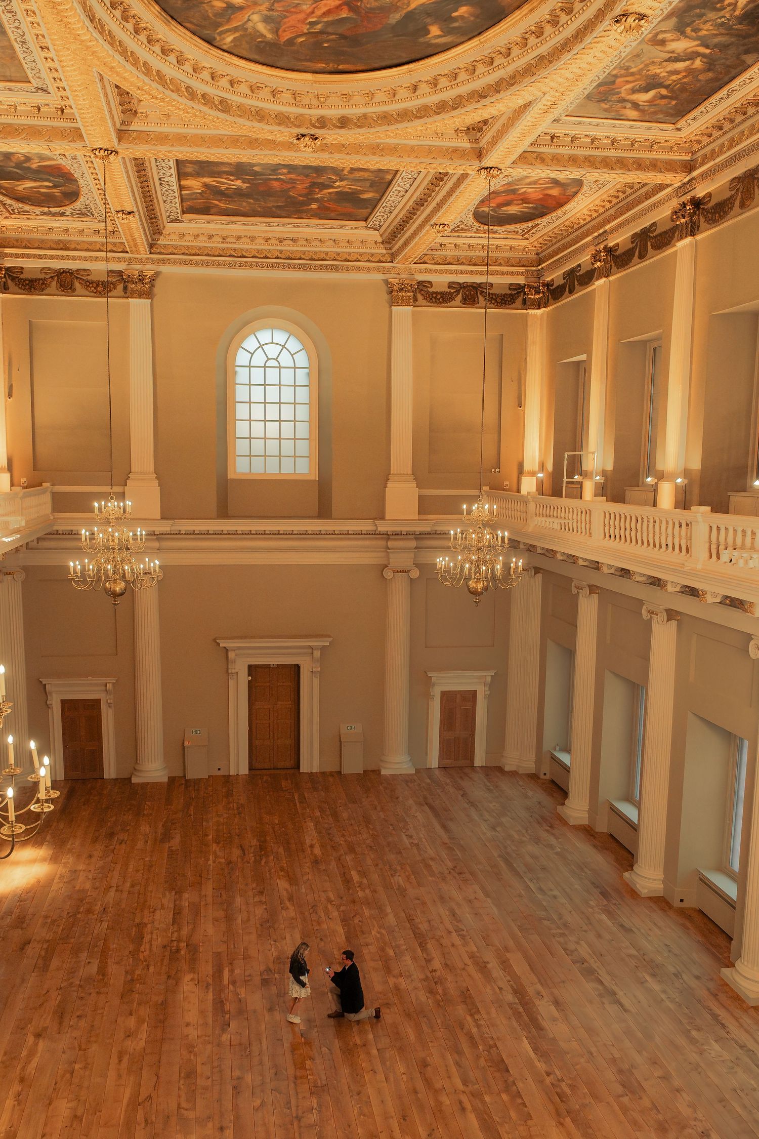 Couple during surprise proposal inside Banqueting House London with grand historic ceiling and wide wooden hall