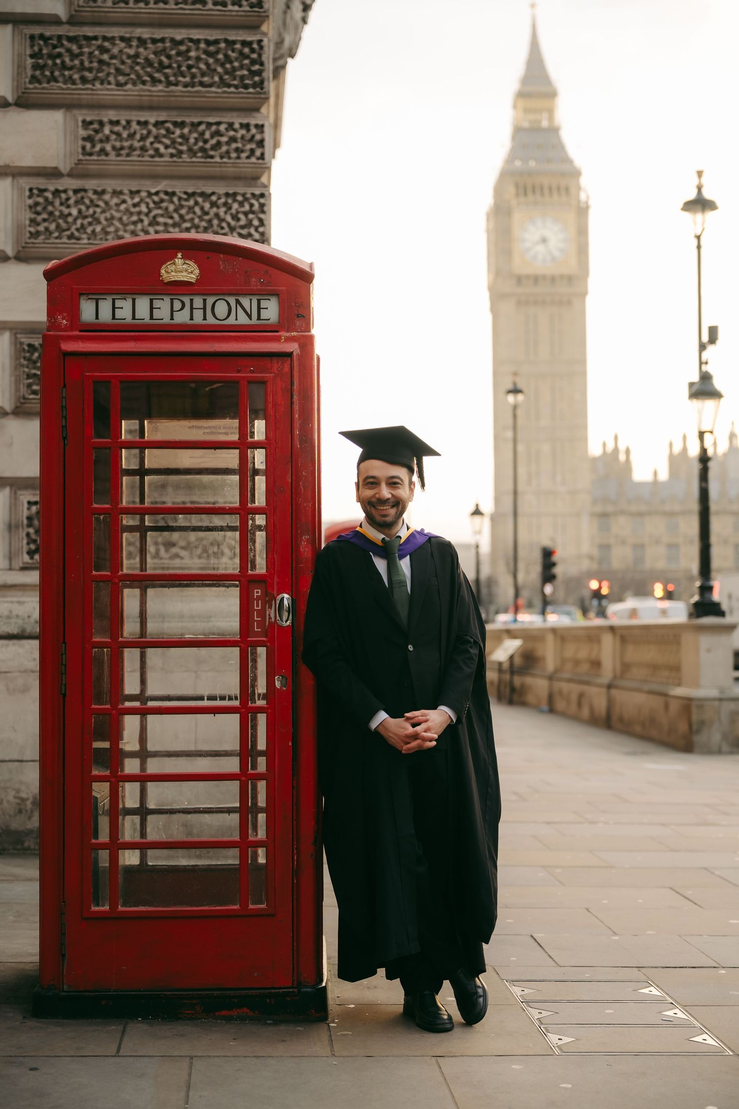 Graduation photos in London by @lyfphotos, Seckin in graduation gown by a red telephone box near Westminster with Big Ben in the background