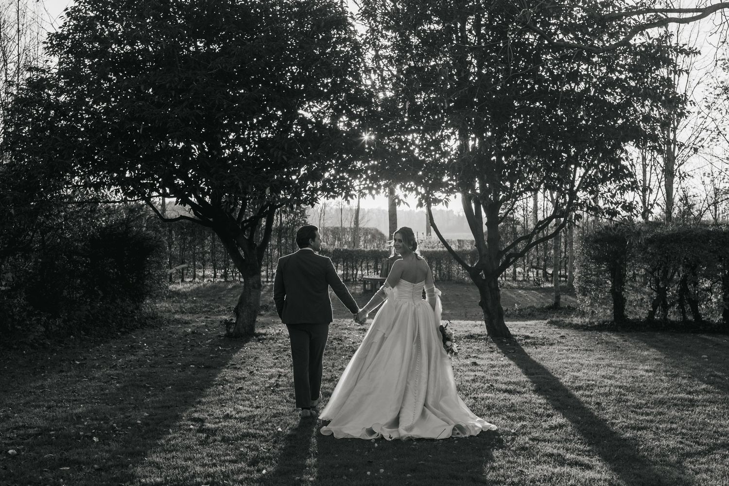 “Black and white photo of the couple walking through the gardens at South Farm Royston, captured by a UK London wedding photographer.”