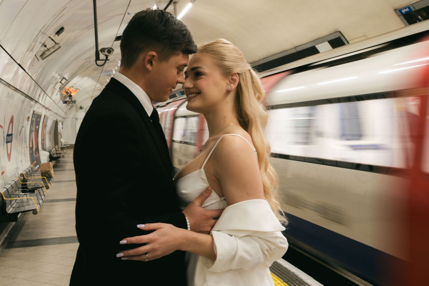 Couple on a London Underground platform with a train passing behind them.