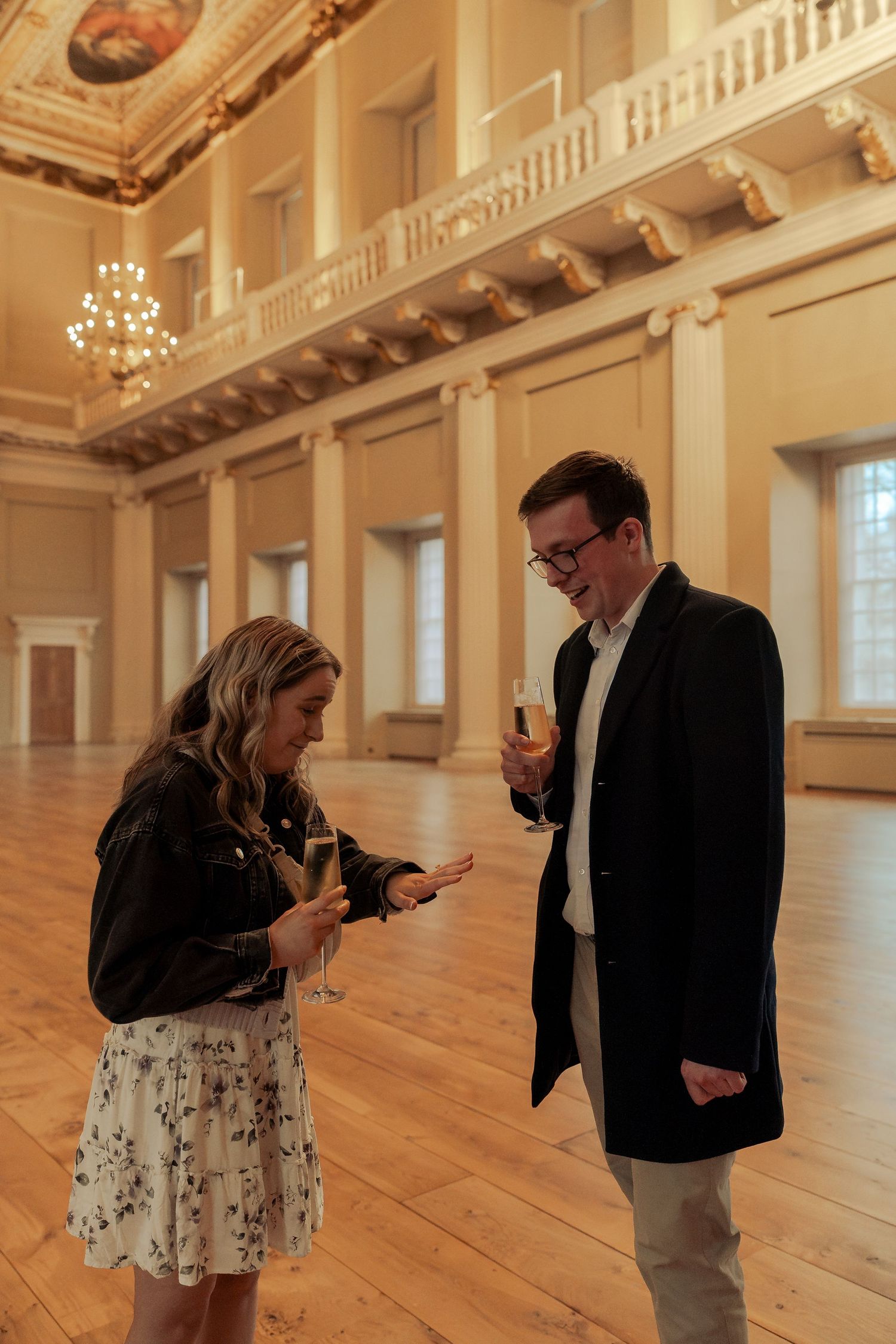 Couple during surprise proposal inside Banqueting House London with grand historic ceiling and wide wooden hall