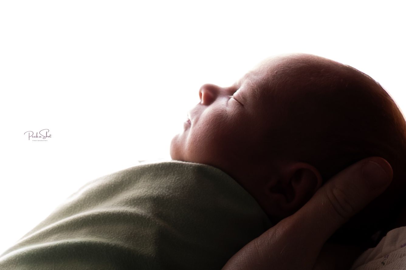 Peaceful newborn baby swaddled in green, cradled in hands against a bright white background.