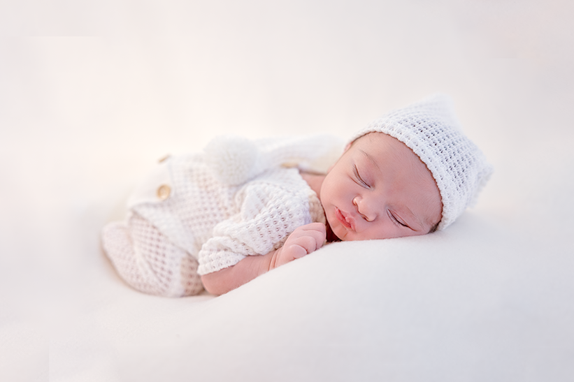Peaceful newborn portrait in white knit outfit on light background.