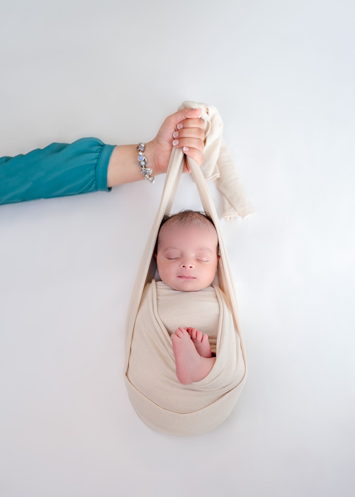 Creative newborn photography series showing baby cradled in beige fabric sling.