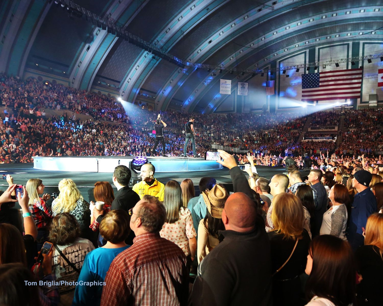 Large concert arena filled with crowd watching performers on stage under dramatic lighting.