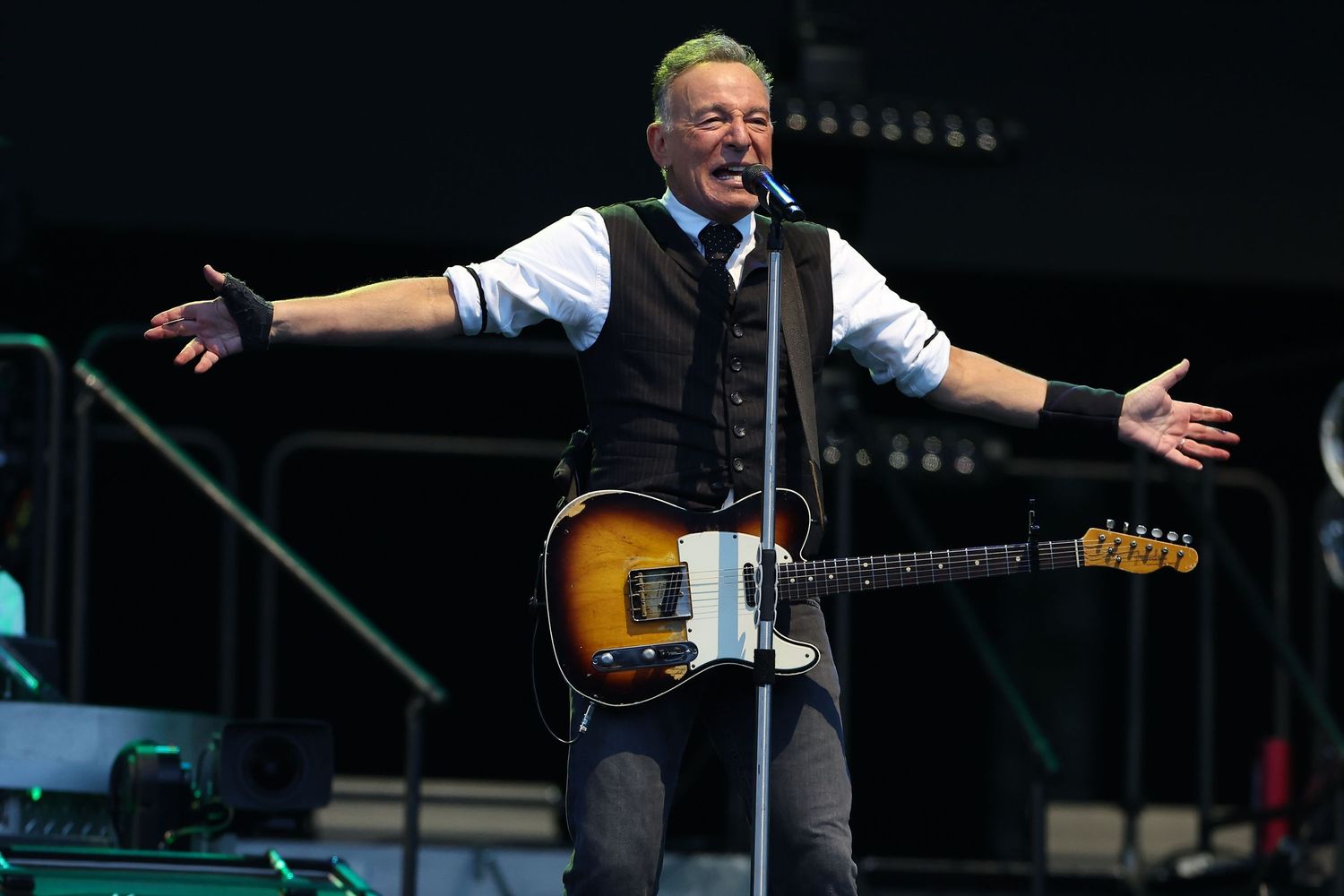 Musician in formal attire playing guitar during outdoor concert performance.