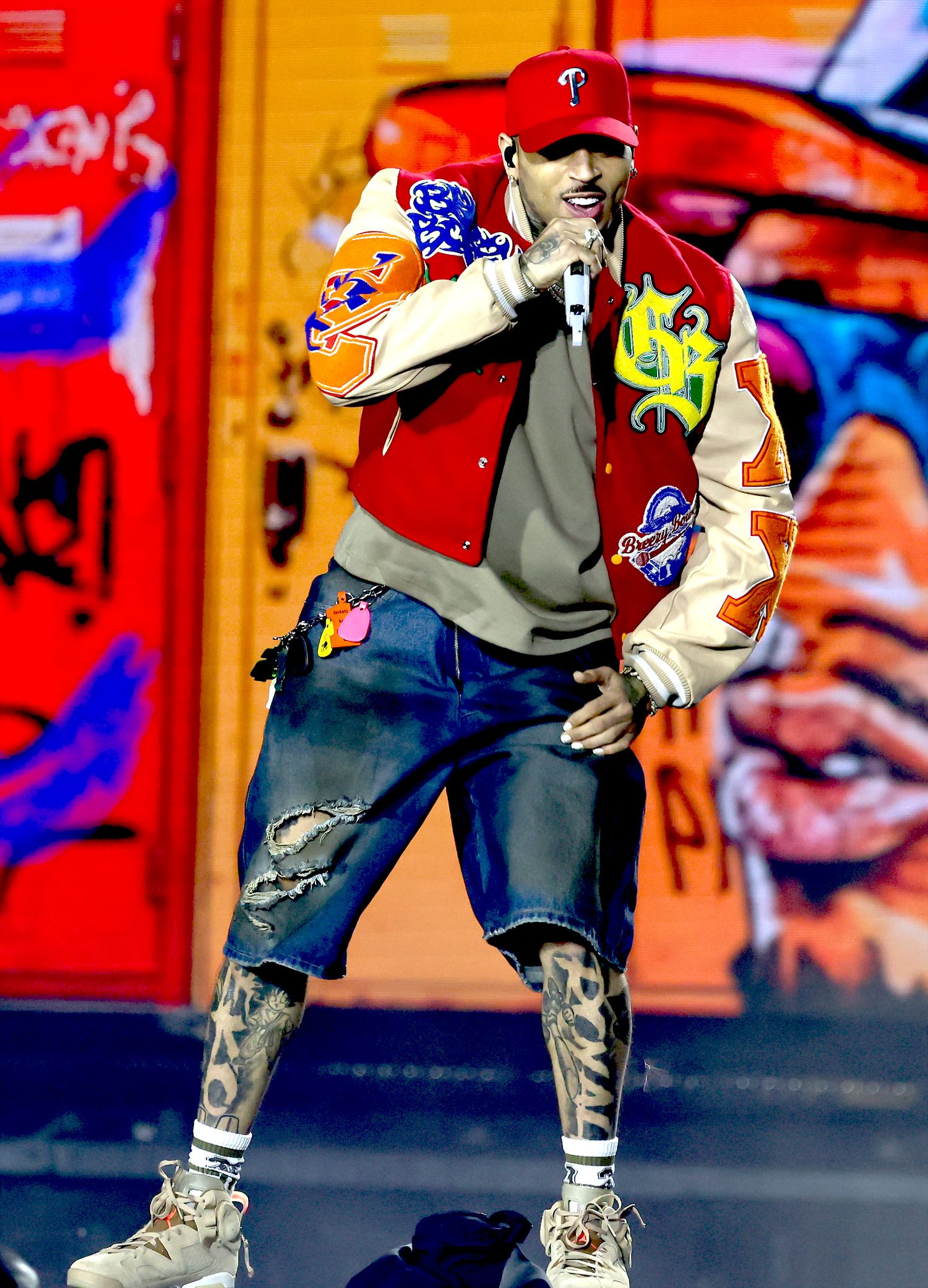 Performer in casual attire and baseball cap dancing on colorful graffiti-style backdrop.
