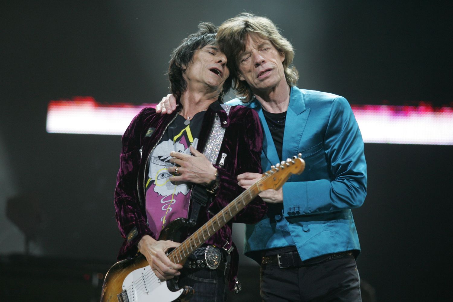 Two guitarists performing together on stage in colorful outfits.