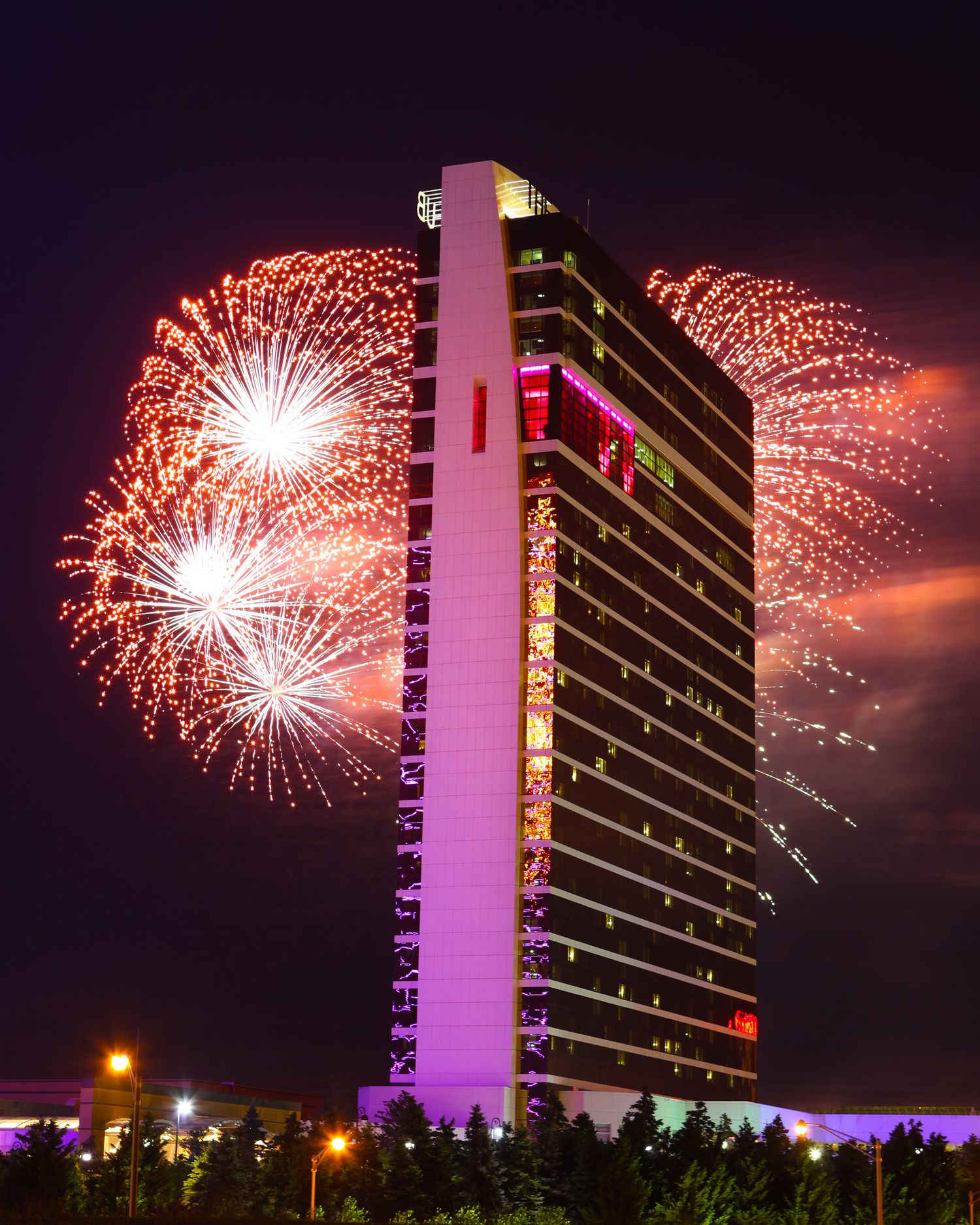 Fireworks display lighting up the night sky behind an illuminated hotel building.