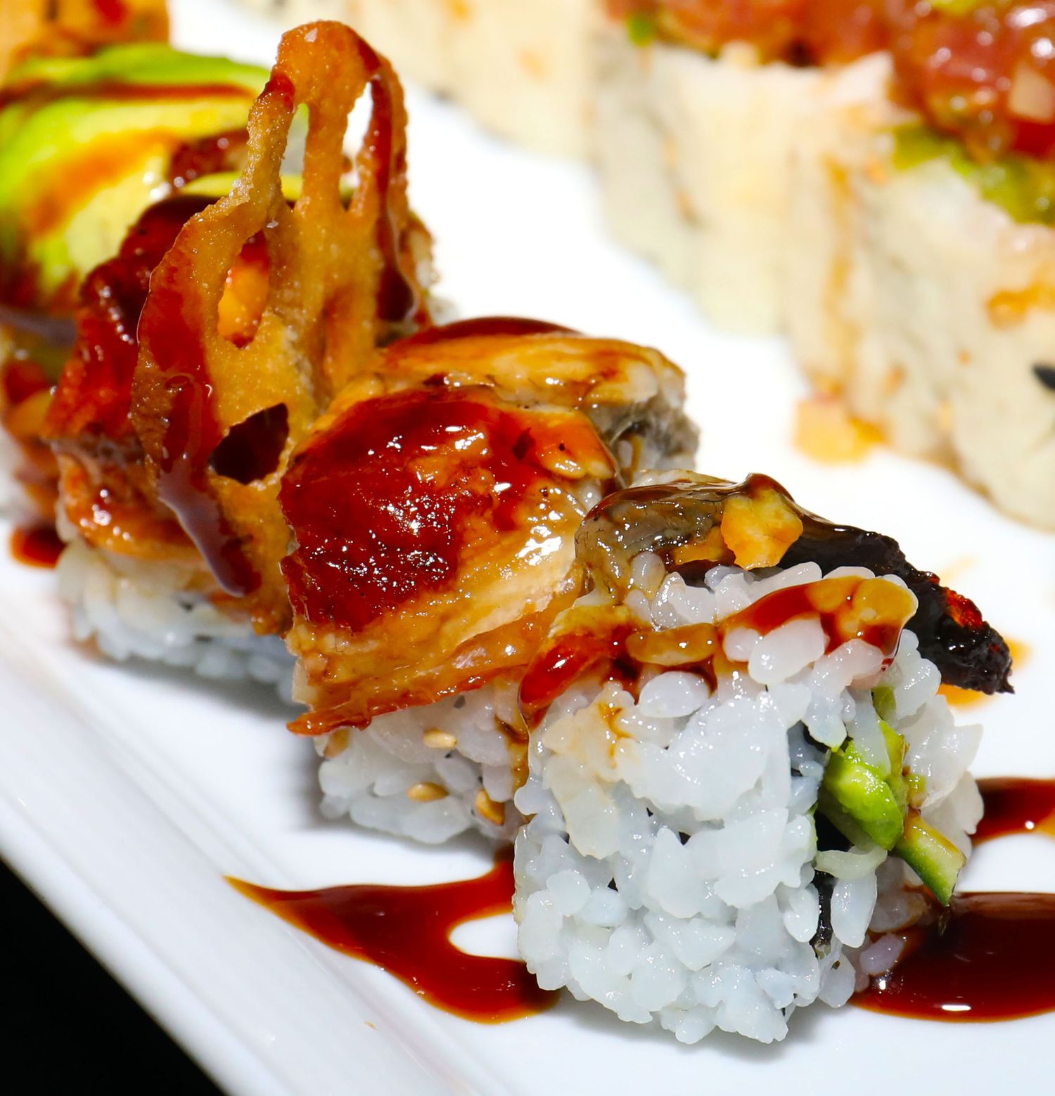 Close-up of sushi rolls topped with glazed meat and sauce on a white plate.