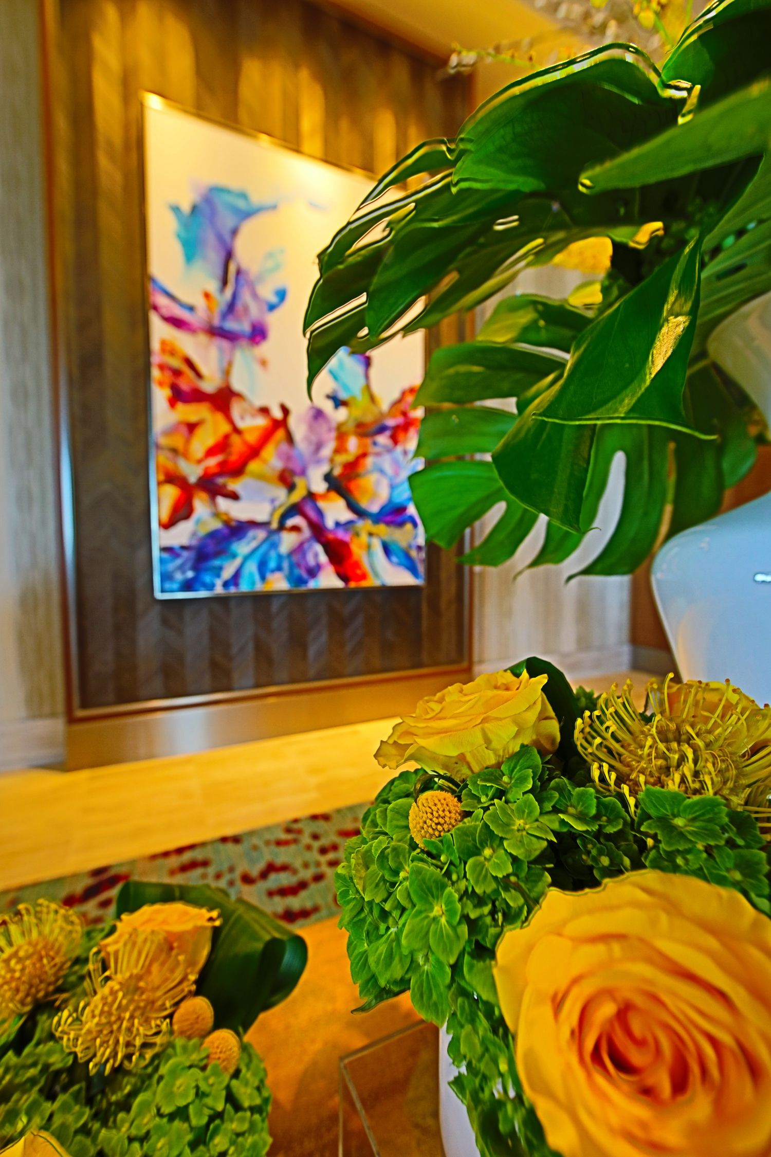 Yellow roses and green foliage arrangement with colorful abstract art on the wall.